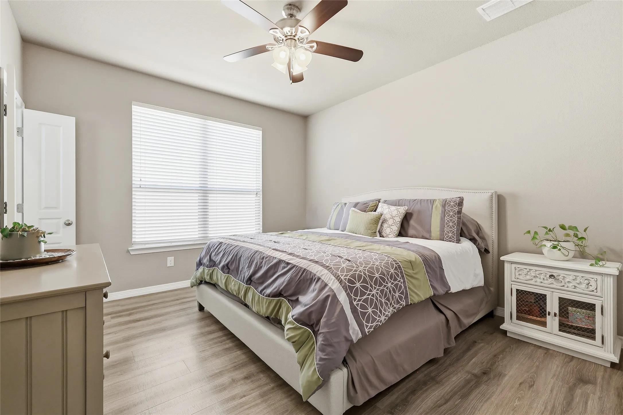 Spacious room featuring vaulted ceilings, a ceiling fan with integrated lighting, wood-finish flooring, and a large window with blinds