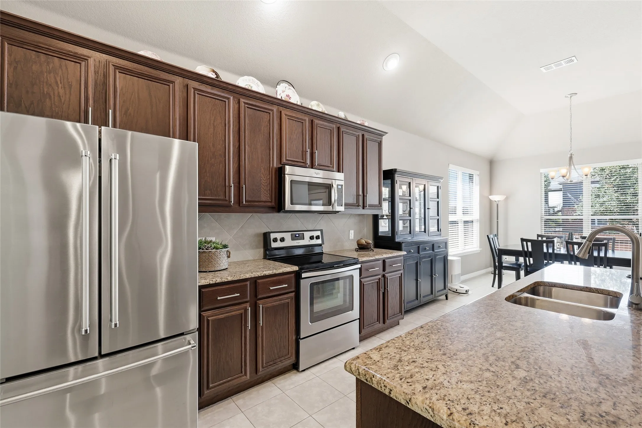 Kitchen featuring wood-finish cabinetry, stainless steel appliances, granite countertops, and tile flooring