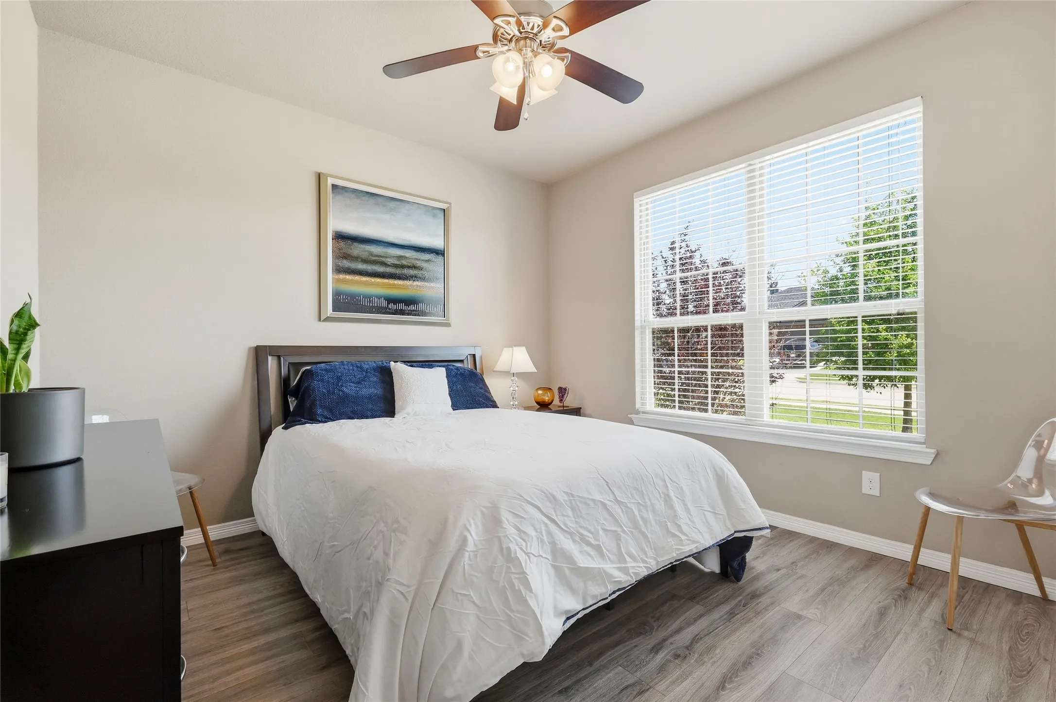 Room featuring a large window with white blinds, wood-finish flooring, and light neutral wall tones