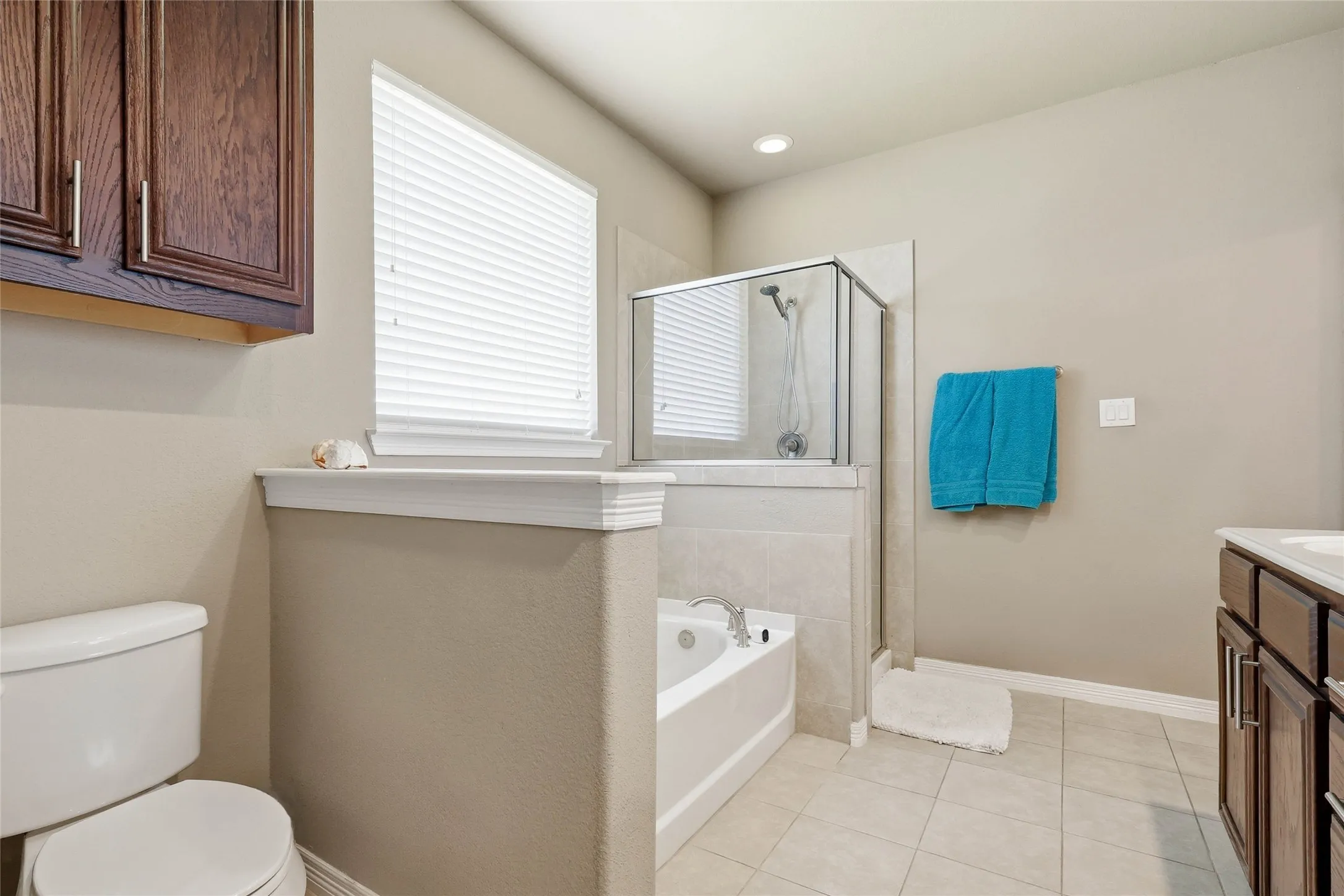 Bathroom featuring a built-in soaking tub, glass-enclosed shower, light-toned tile flooring, recessed lighting, and a dark wood-finish vanity with a white countertop