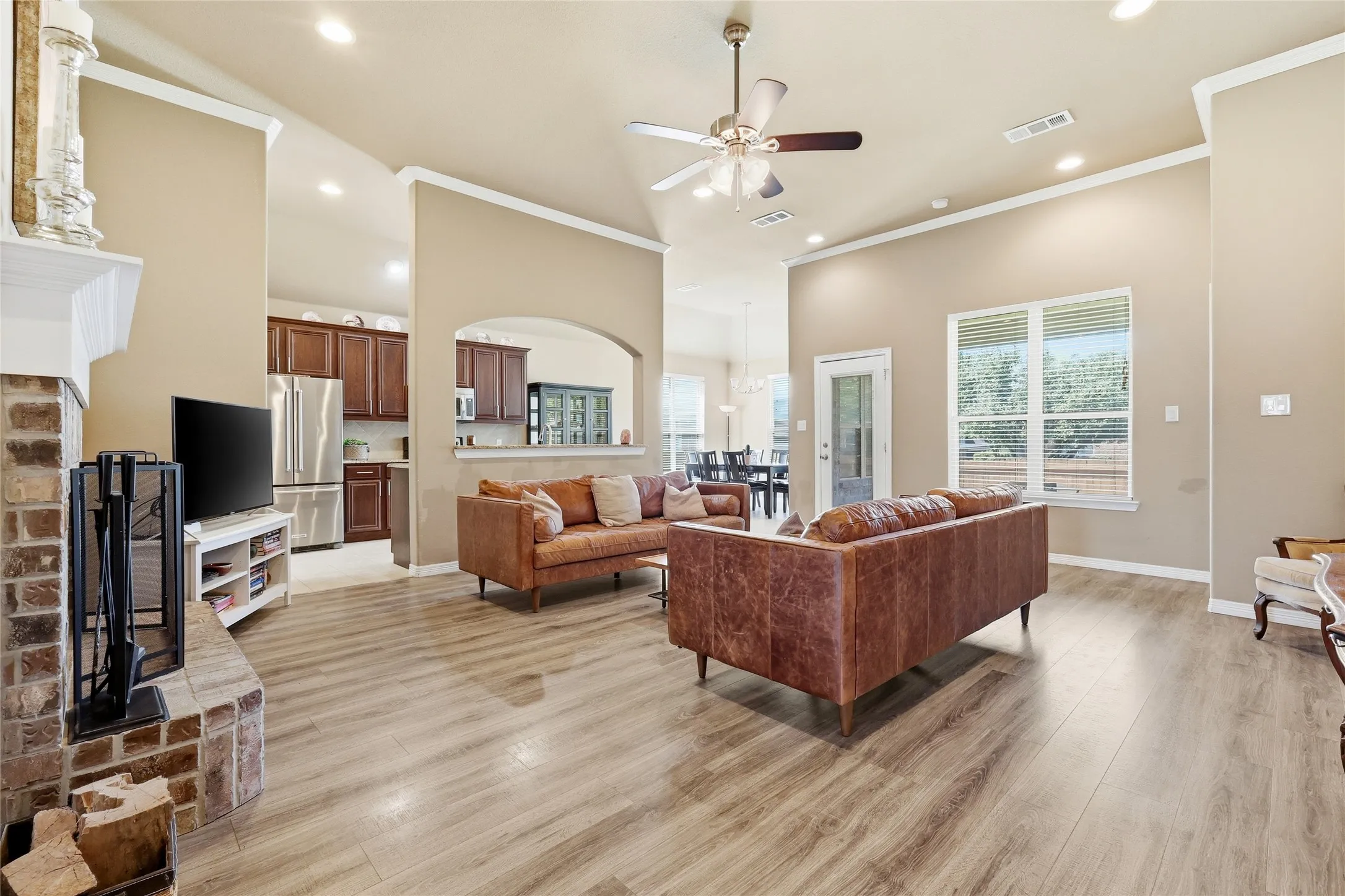 Living area featuring high ceilings, wood-finish flooring, a brick fireplace with a white mantle, an arched doorway, and recessed lighting