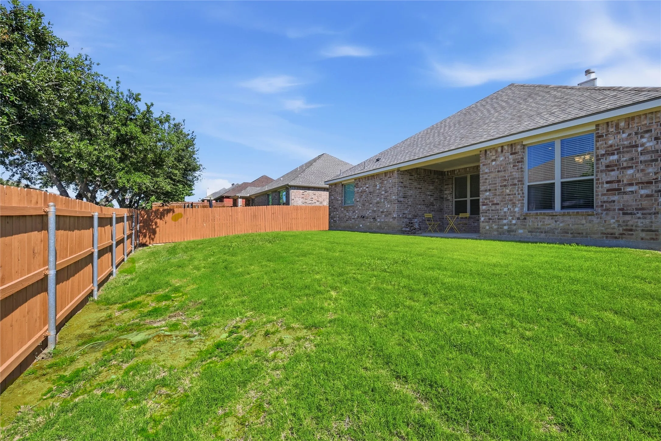 Expansive backyard featuring a manicured lawn, wood privacy fencing, and mature trees