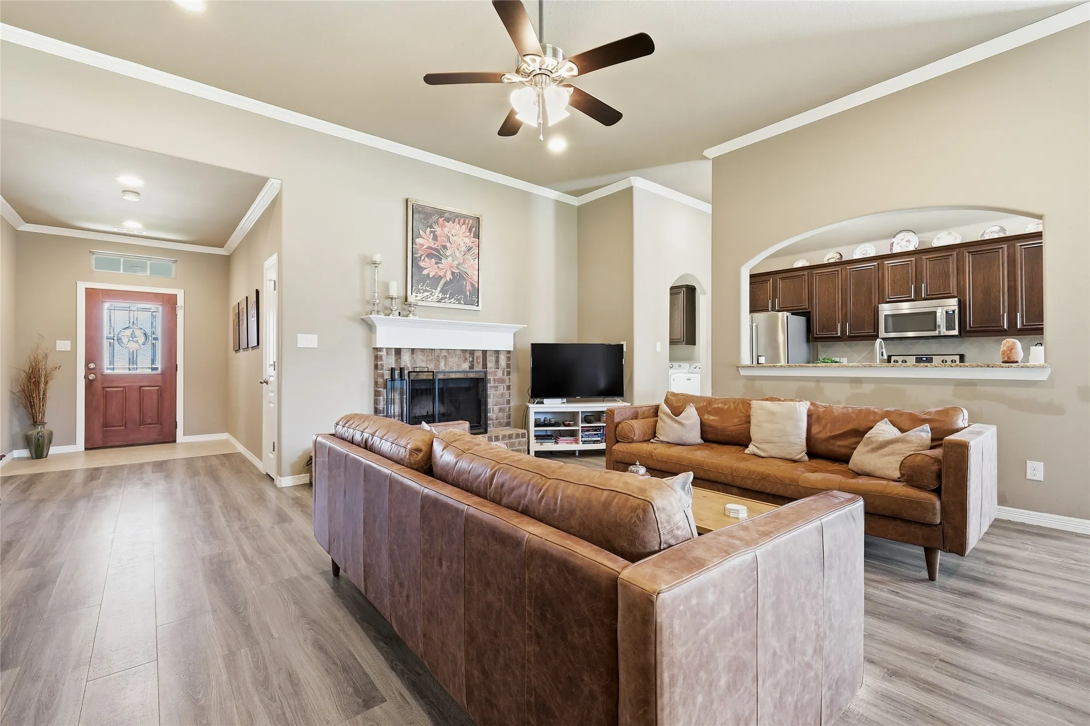 Spacious living area featuring wood-finish flooring, a brick fireplace with a white mantel, and crown molding