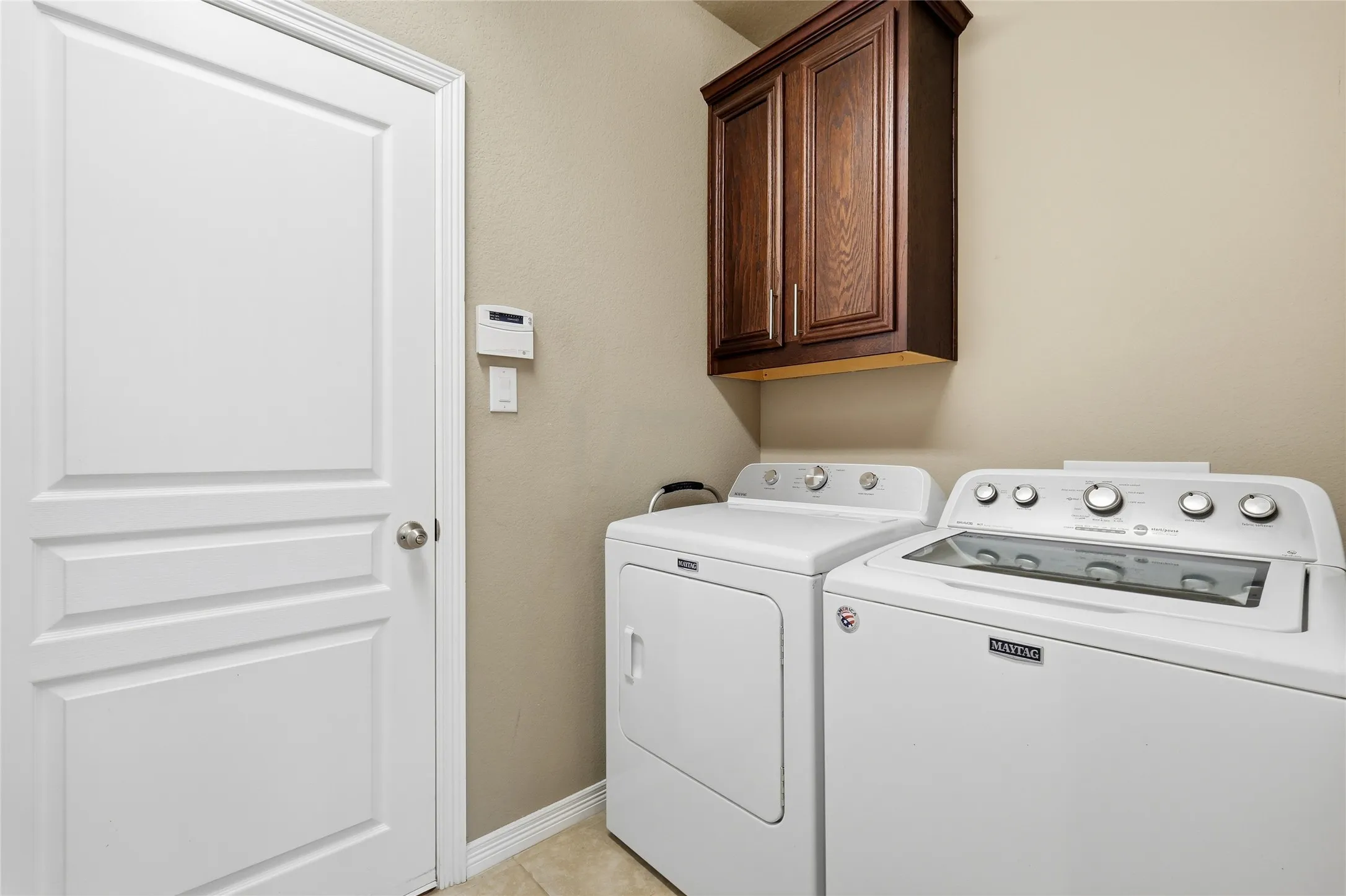 Dedicated utility space featuring overhead wood cabinetry and tile flooring