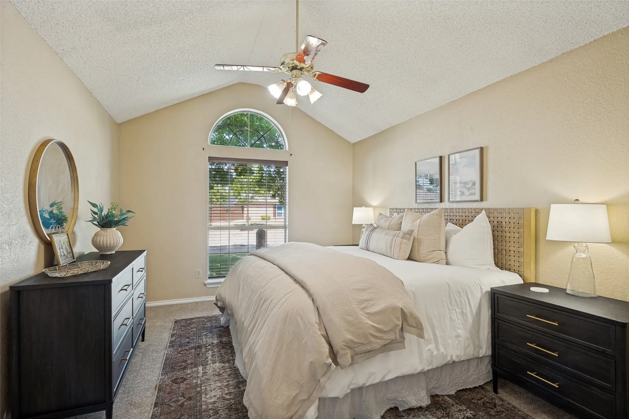 Primary Bedroom: Vaulted ceiling with ceiling fan, arched transom window, and carpeted flooring