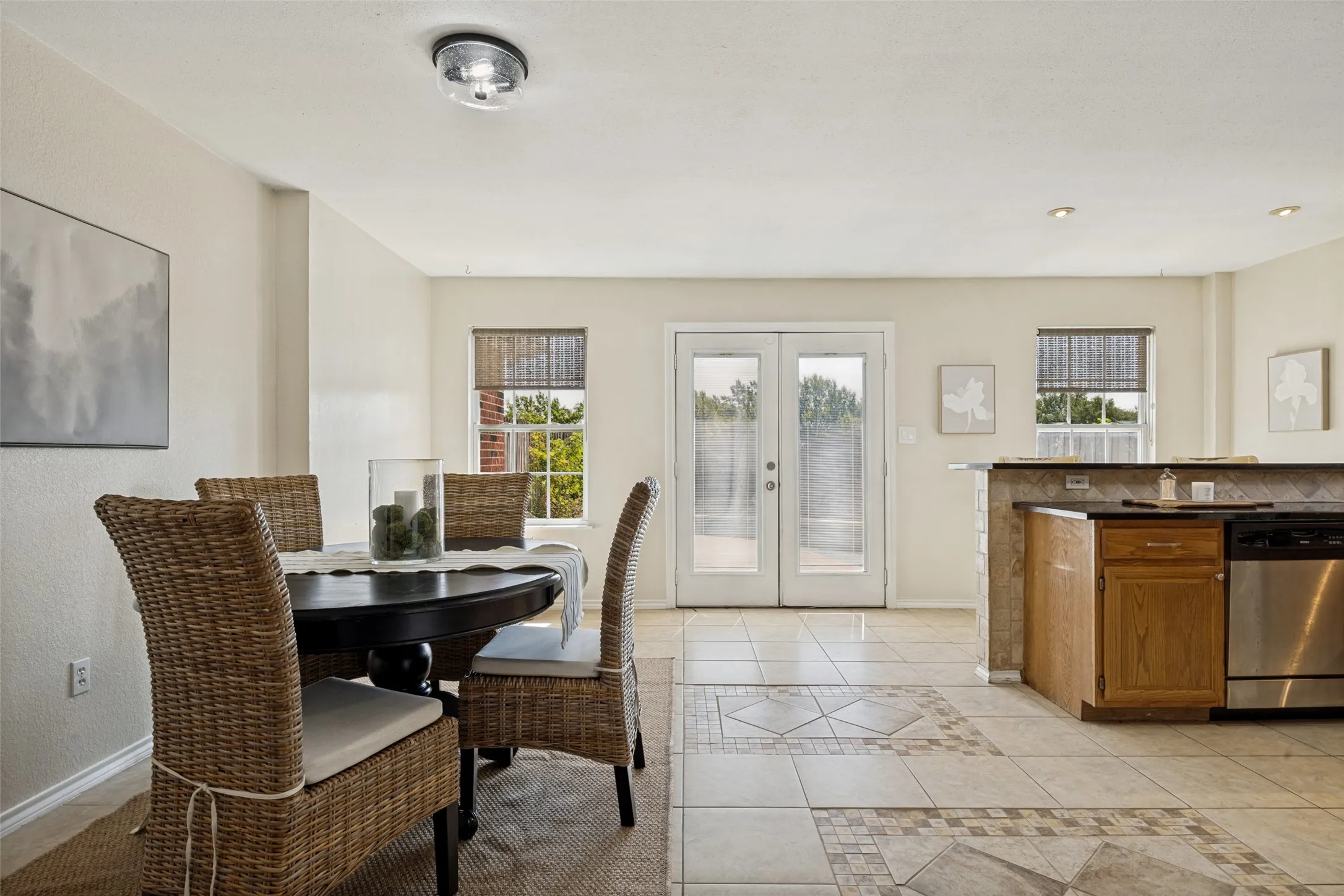 Ceramic tile flooring, white walls, double French doors, light wood cabinetry, and stainless steel appliances