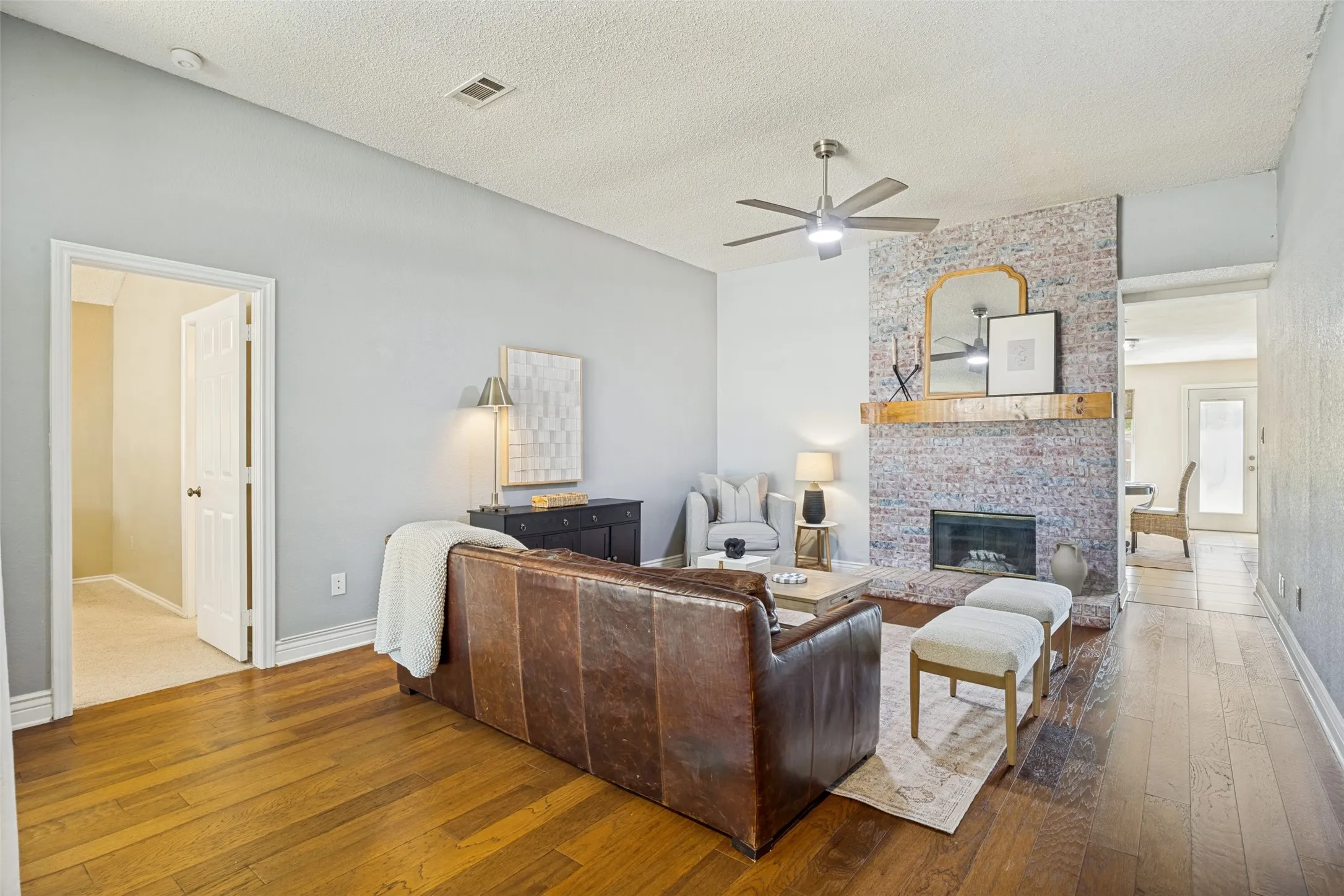 Hardwood-finish flooring, a ceiling fan with integrated lighting, a brick fireplace, a wood mantel, and crisp white trim