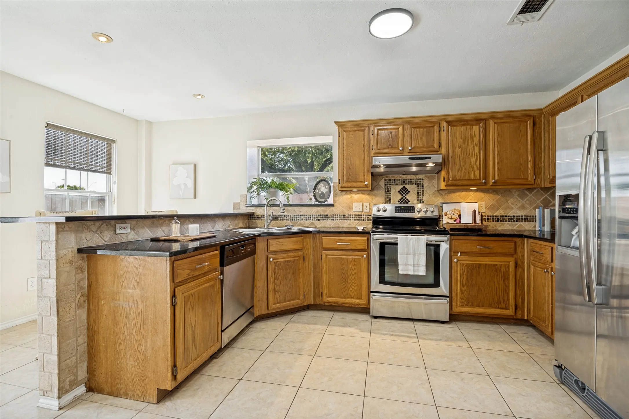 Kitchen featuring wood cabinetry, black countertops, stainless steel appliances, and a tiled backsplash
