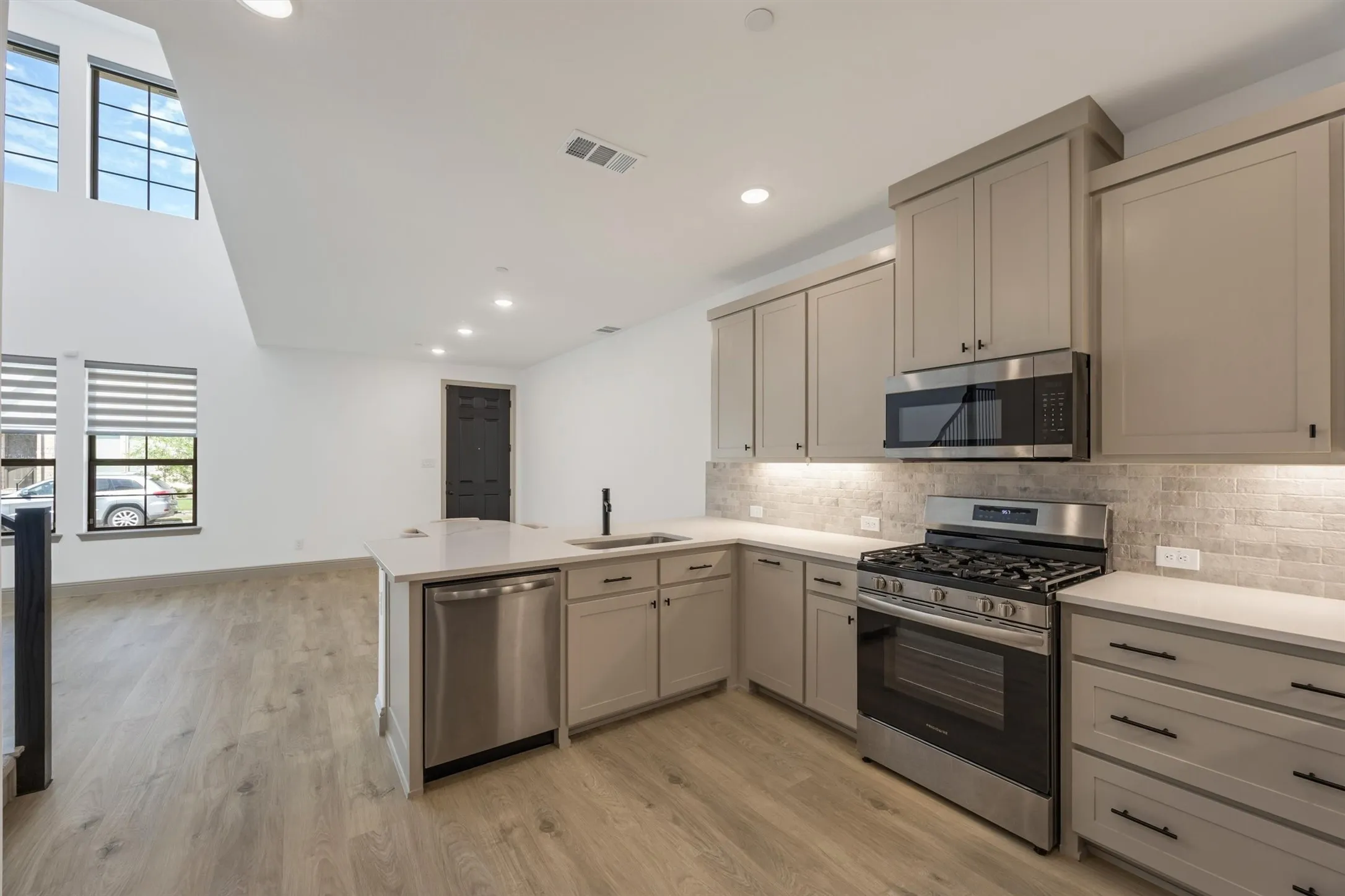 Open-concept kitchen featuring light-toned cabinetry, stainless steel appliances, a center island with sink, and light wood-finish flooring