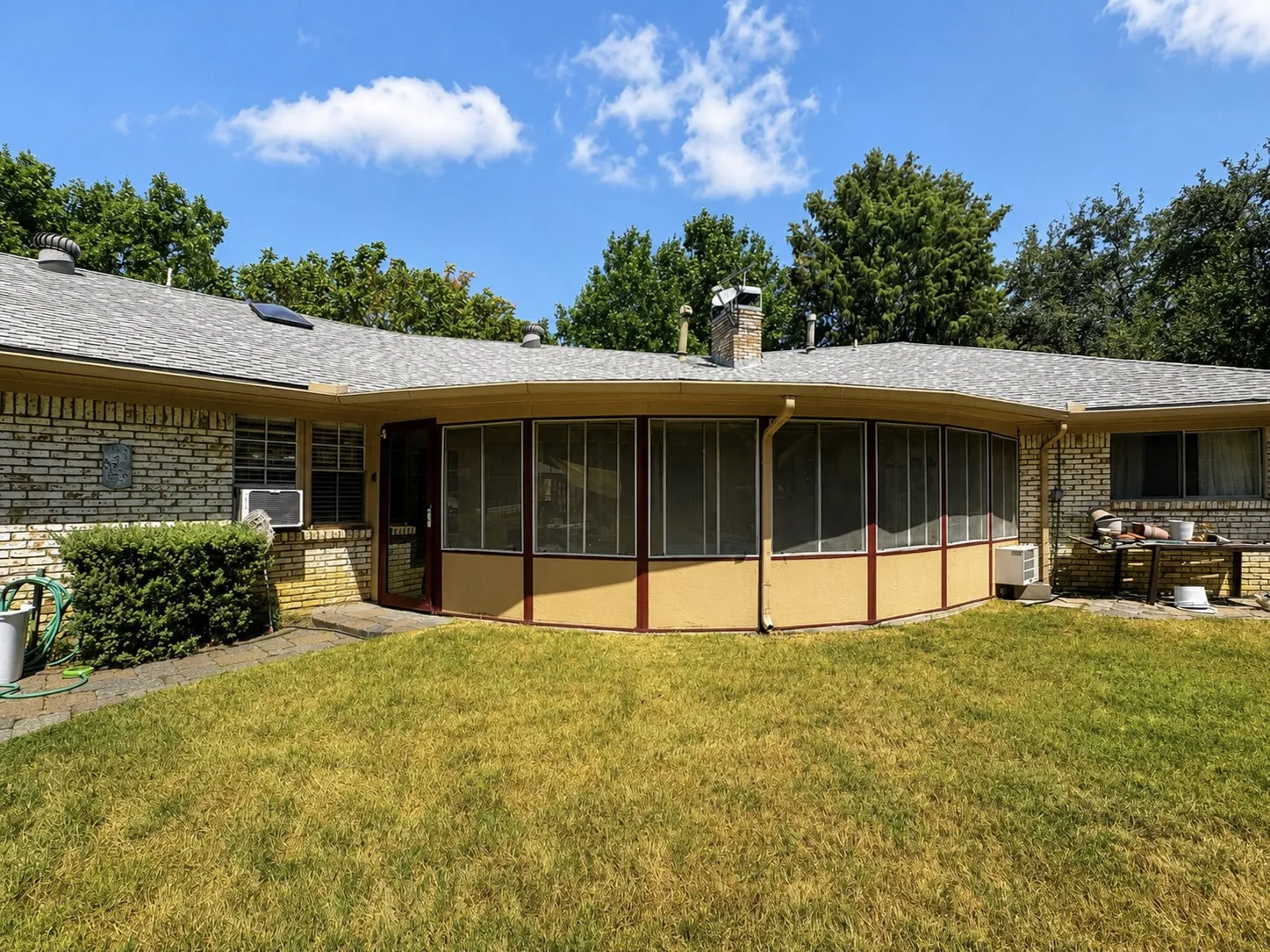 Curved screened sunrom with a shingle roof, brick exterior, and a stone chimney