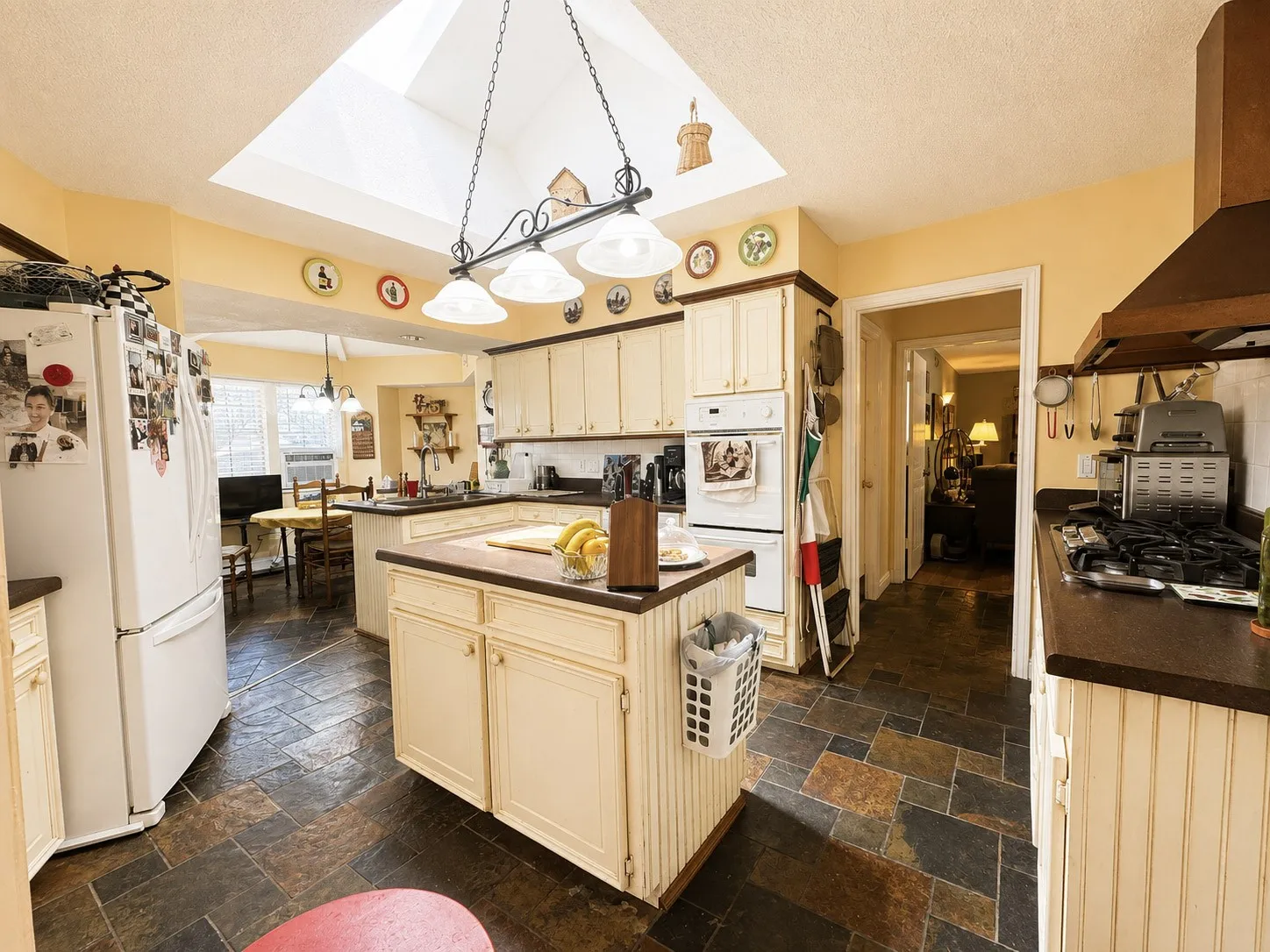 Kitchen featuring a central island, skylight, slate tile flooring, off-white cabinetry, and integrated double ovens