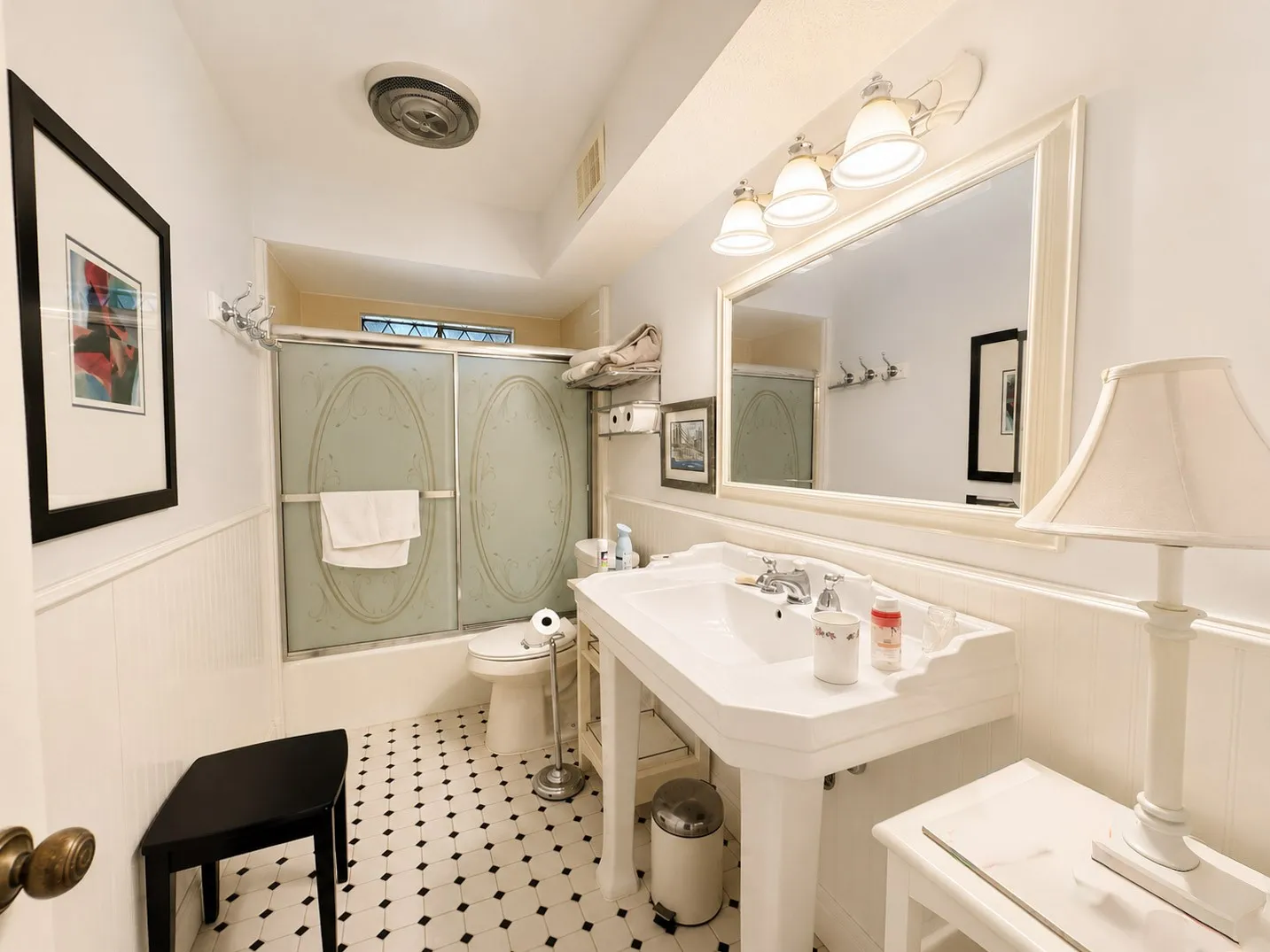 White beadboard wainscoting, black and white checkered floor tiling, a pedestal sink, and a framed vanity mirror with overhead lighting