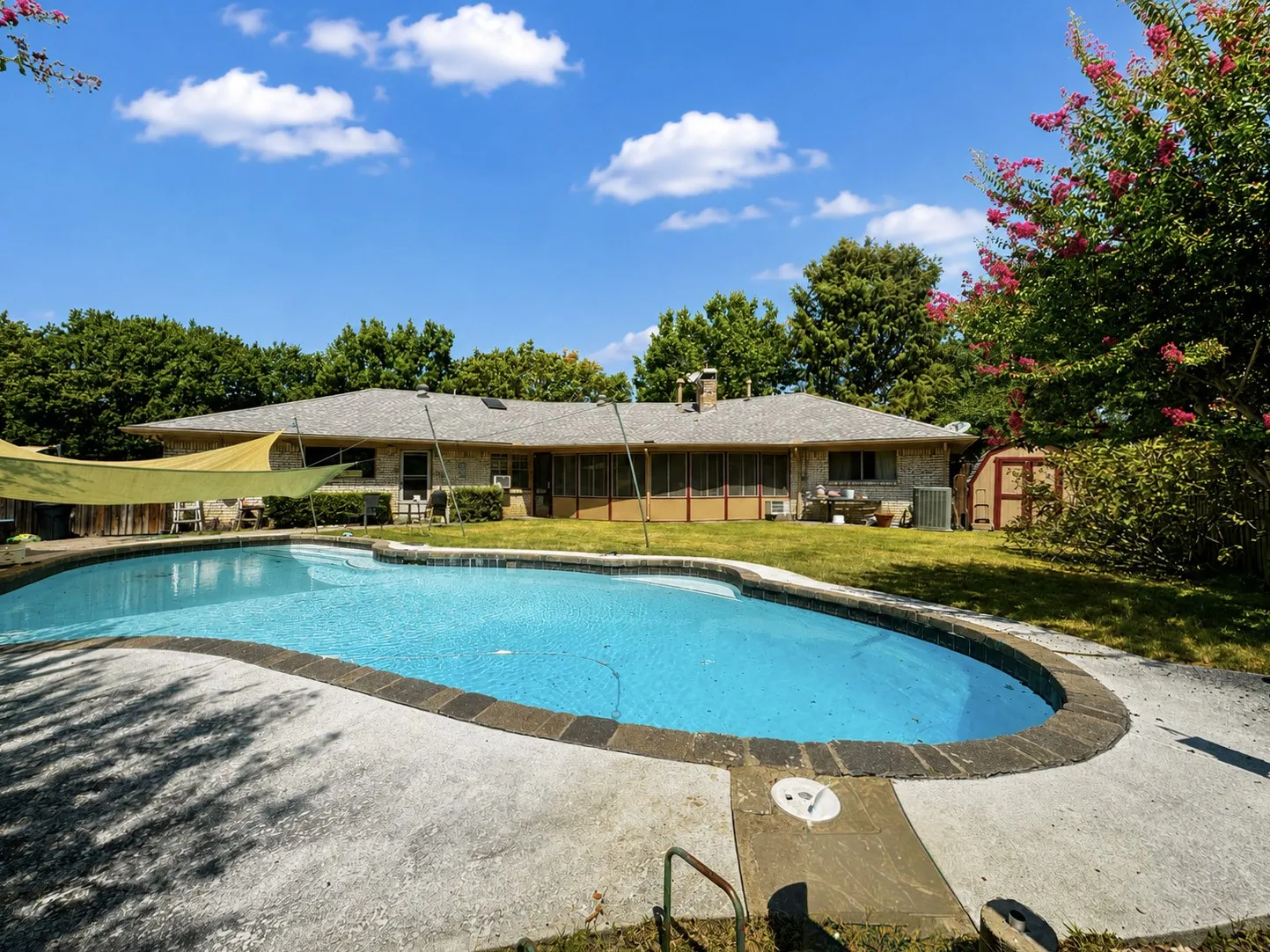 Resort-style backyard featuring a freeform swimming pool with stone coping, concrete decking, and mature trees