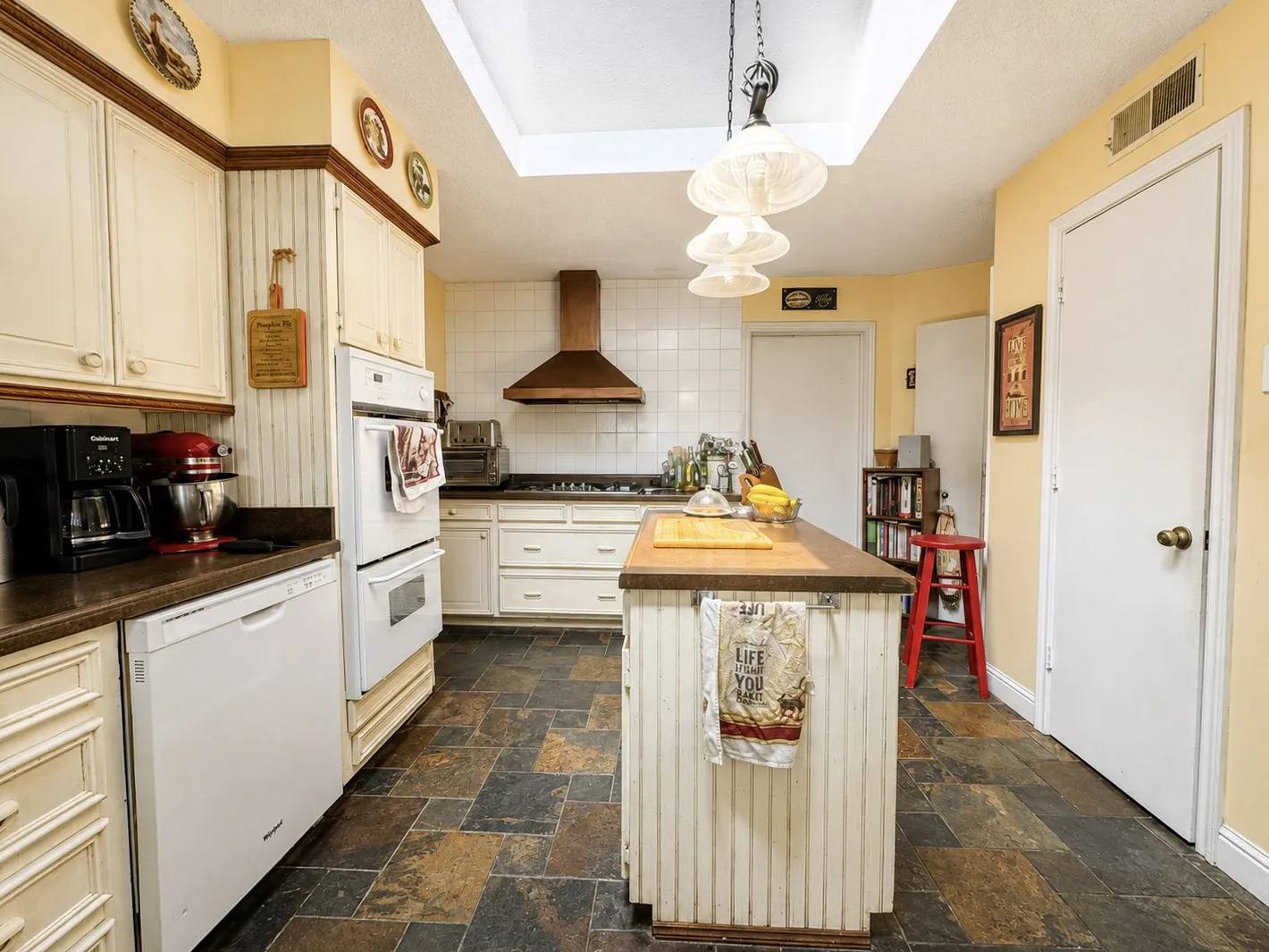 Kitchen featuring a skylight, pendant lighting, white cabinetry, integrated double oven, and stone tile flooring