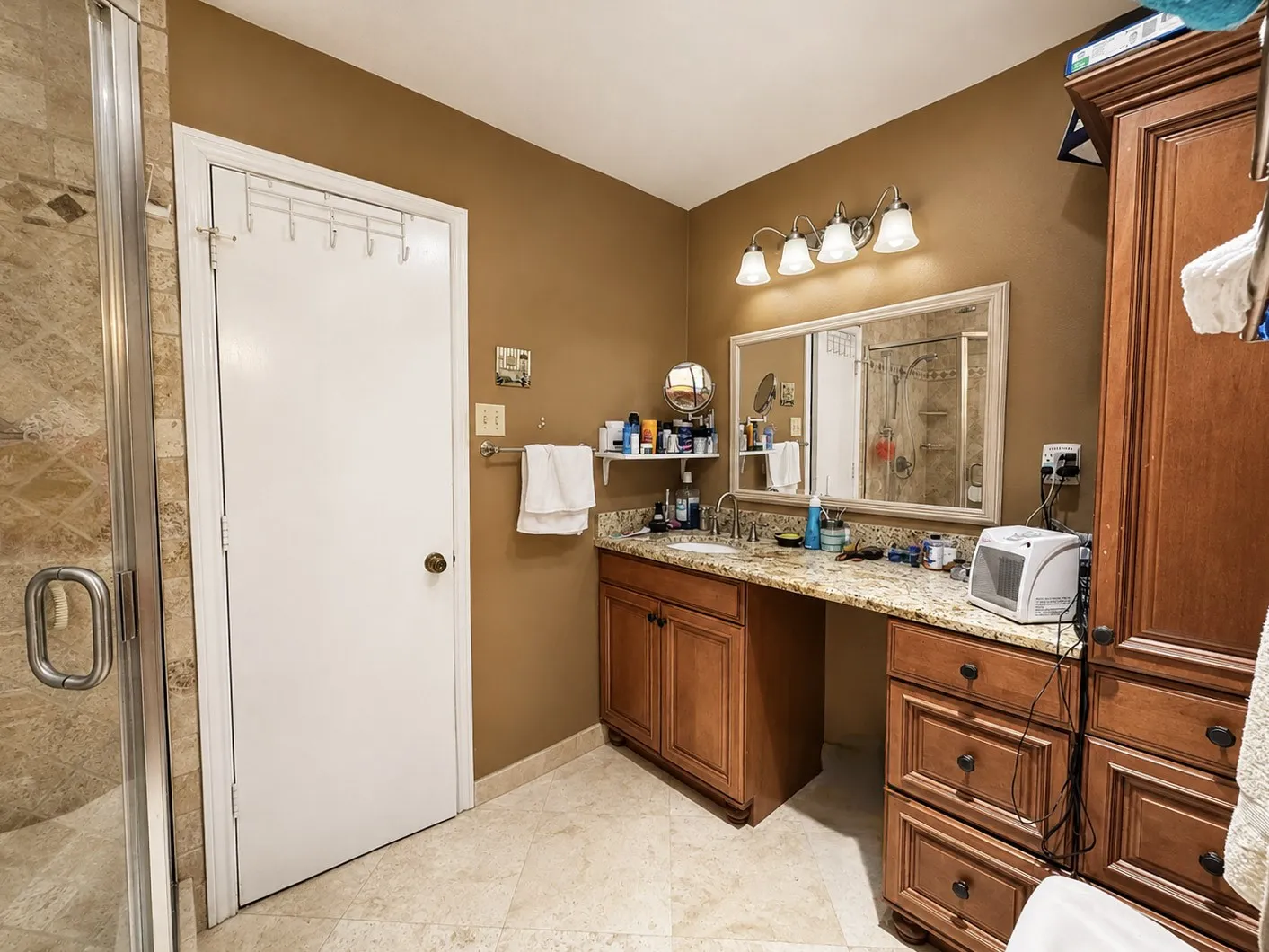 Tile flooring, an enclosed shower with tile surround, a vanity with an integrated sink, a stone-finish countertop, and wood-finish cabinetry