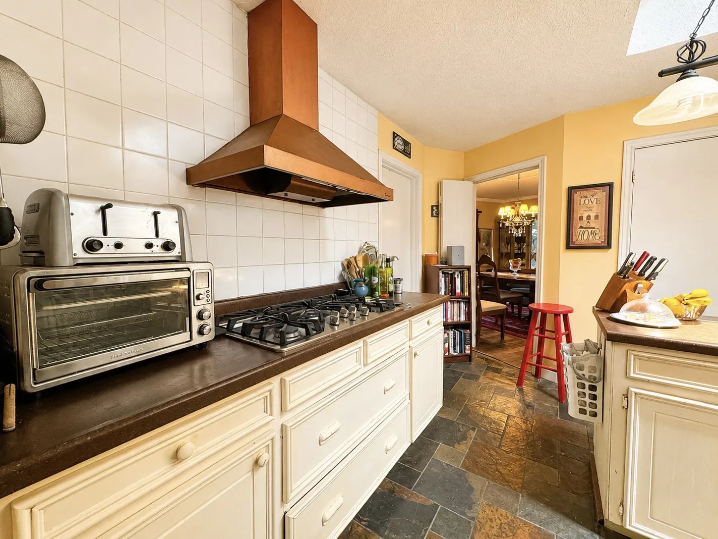 Kitchen featuring a gas range, copper range hood, white tile backsplash, dark countertops, and slate flooring