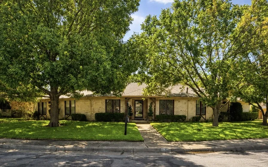 Brick exterior with dark trim windows, mature trees, manicured lawn, and paved walkway