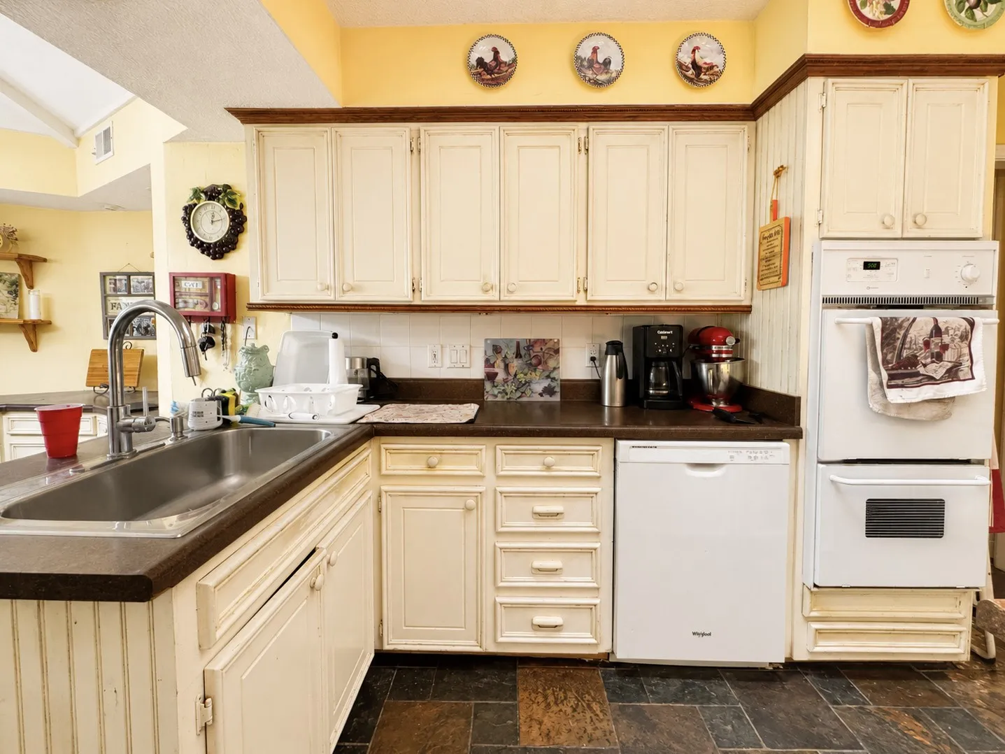 Cream-finished cabinetry with wood trim, stainless steel sink with gooseneck faucet, built-in double oven, and integrated dishwasher