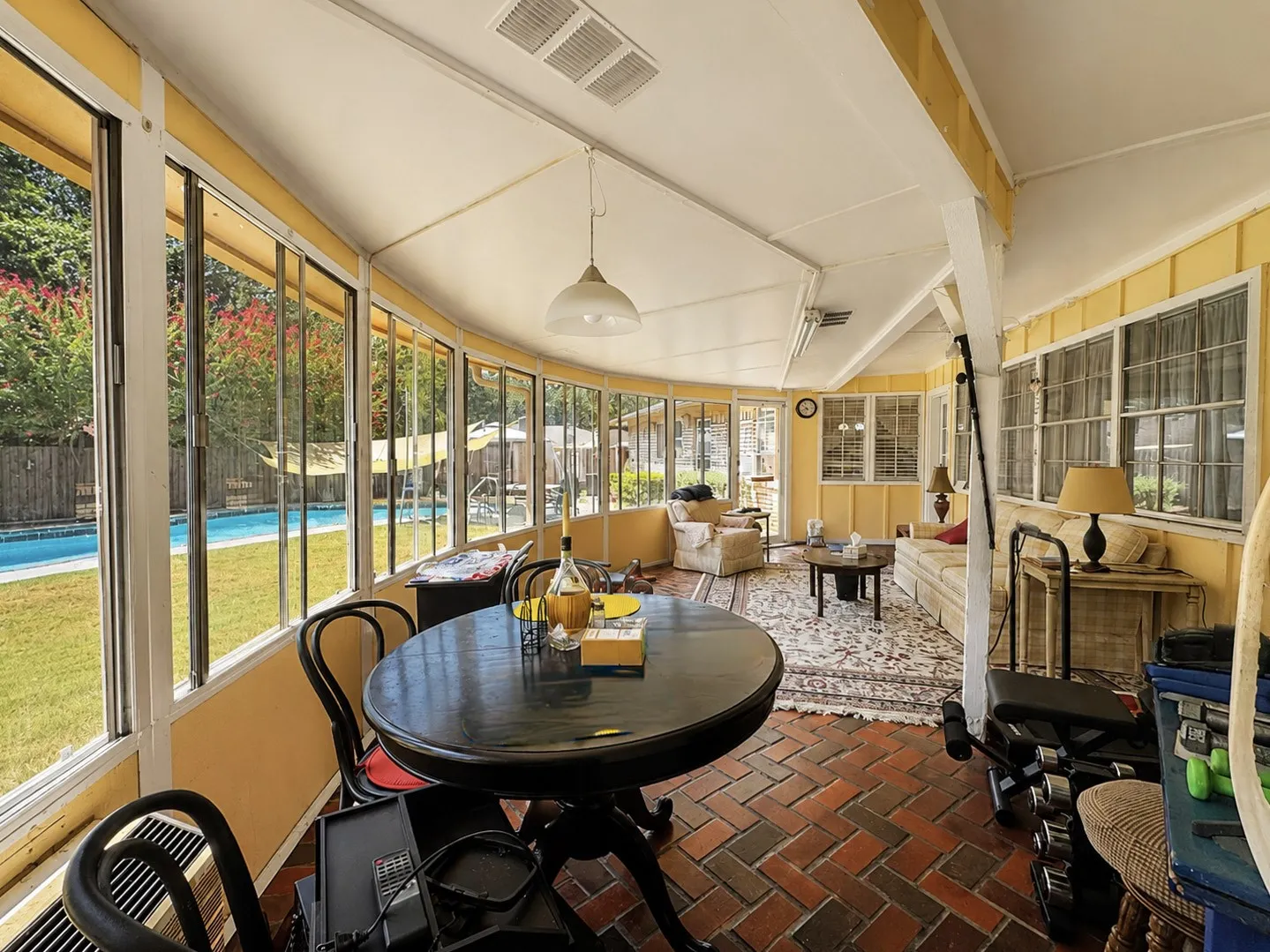 Enclosed sunroom featuring a brick-patterned floor, full-height windows, a vaulted ceiling, and an integrated ceiling light fixture