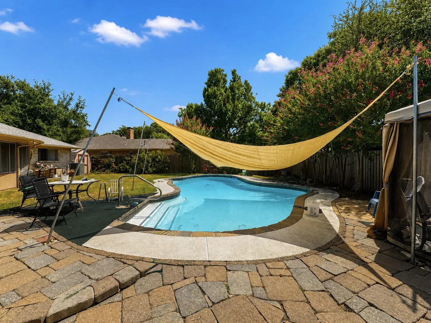 Freeform swimming pool with integrated steps, surrounded by a flagstone-style paver patio and concrete decking