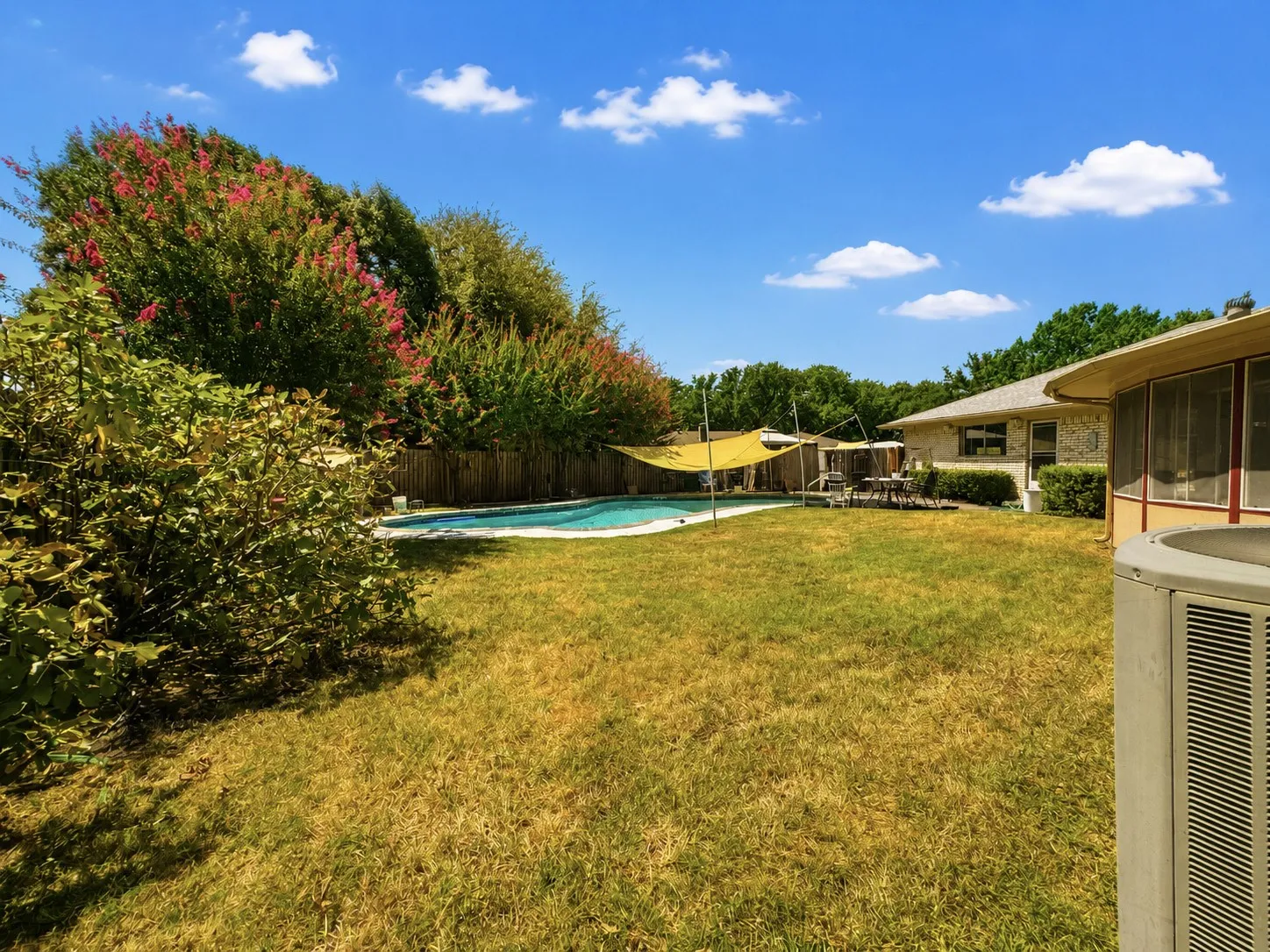 Expansive backyard featuring a swimming pool, partial privacy fencing, and mature trees with pink blossoms