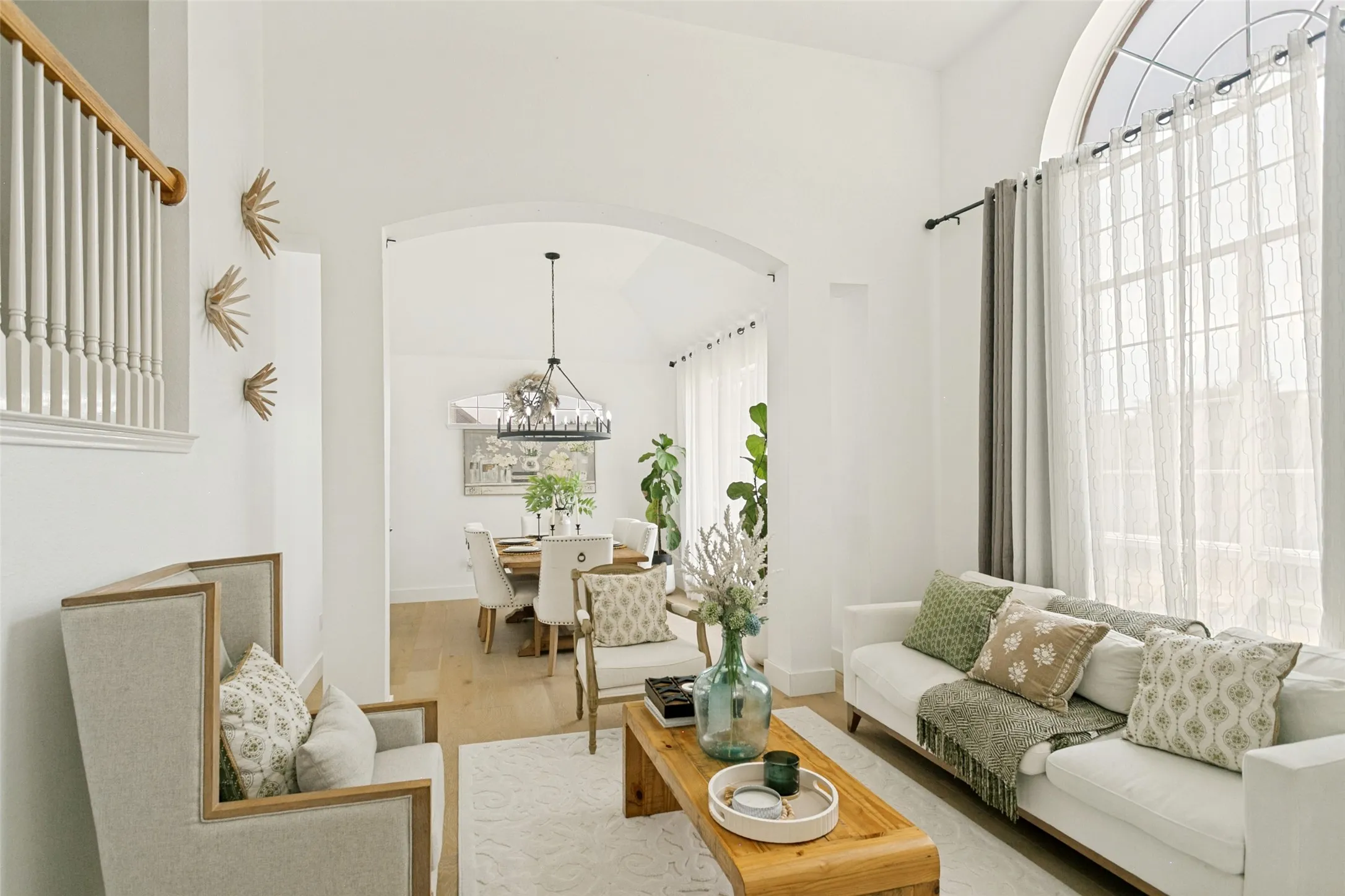 High ceilings with a prominent arched window, wood-finish flooring, and an elegant chandelier
