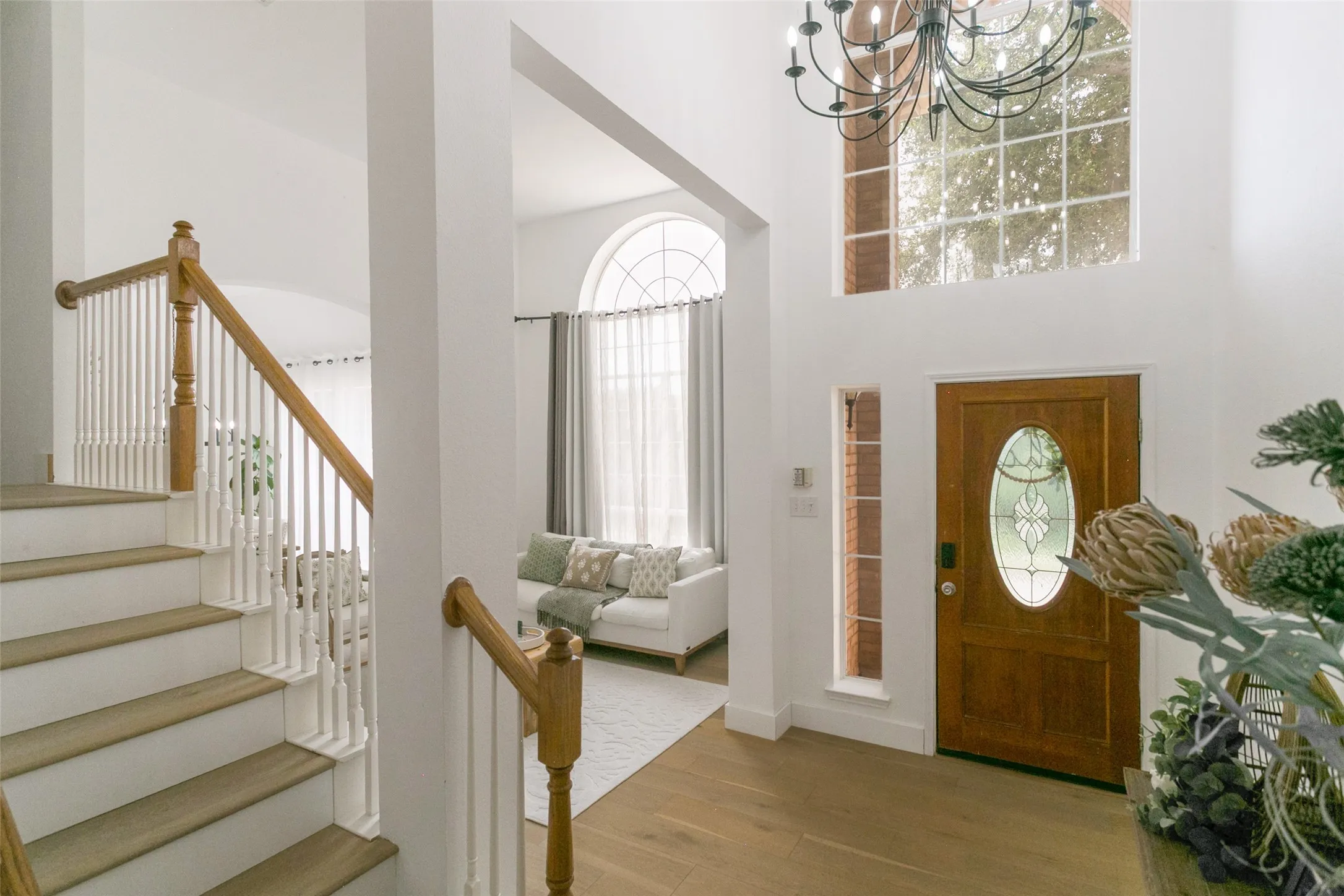 Two-story entryway with wood-finish flooring, a wood front door with decorative glass, and a large multi-pane window