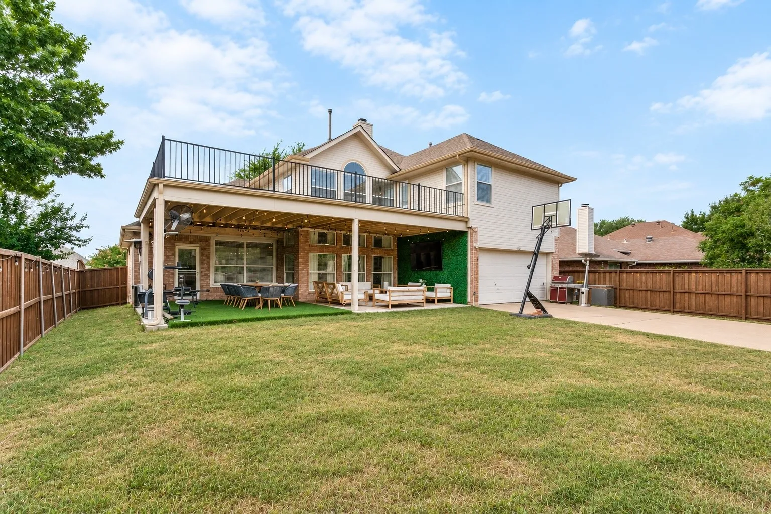 Expansive backyard featuring a covered patio, artificial turf area, and a second-story balcony with metal railings