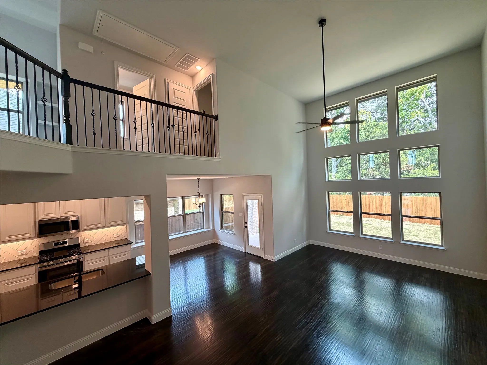 Impressive Great Room with a wall of windows with view of trees, rich hardwoods, and elegant wrought iron staircase