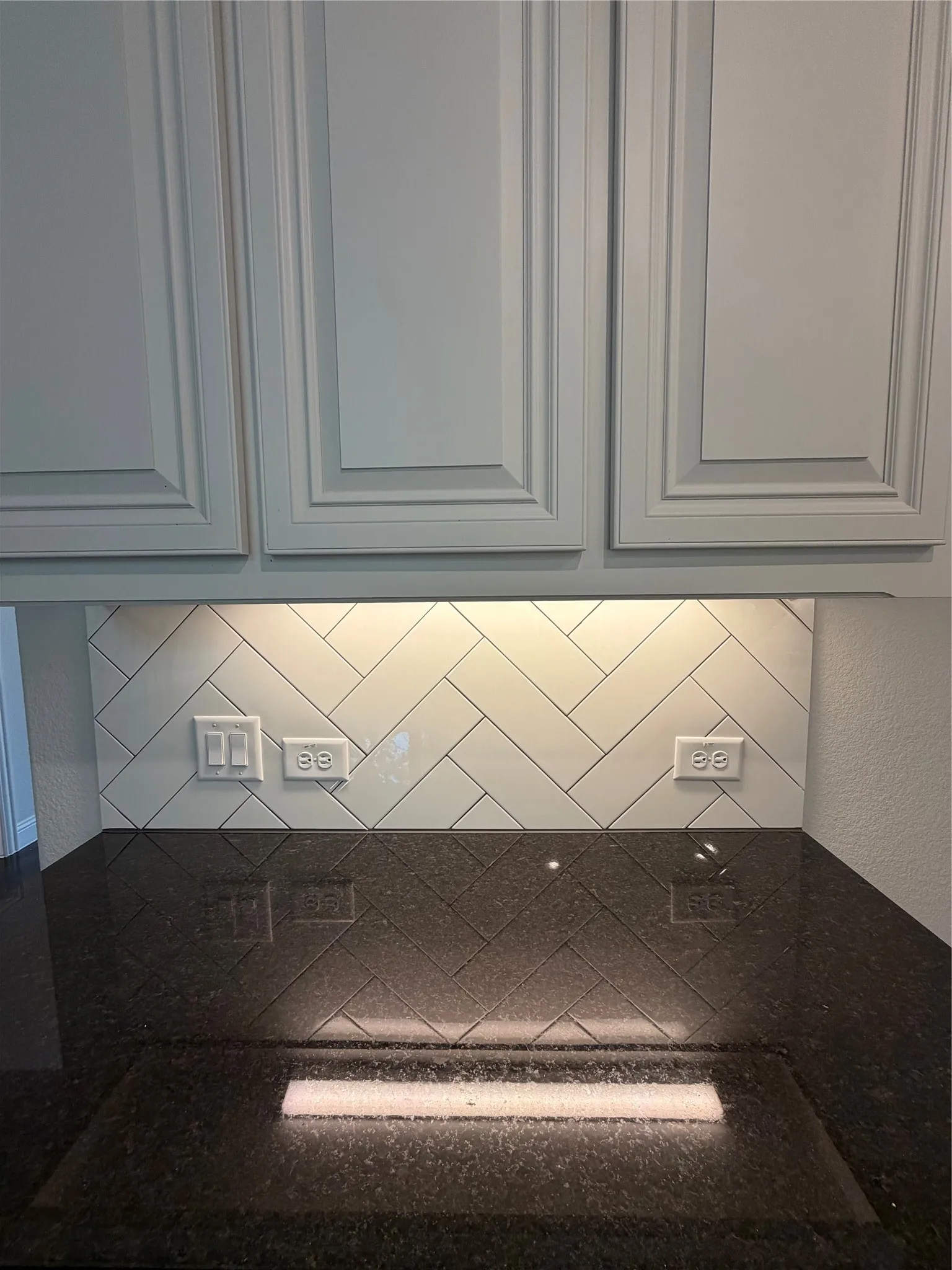 Close up of herringbone patterned white backsplash and undercabinet lighting