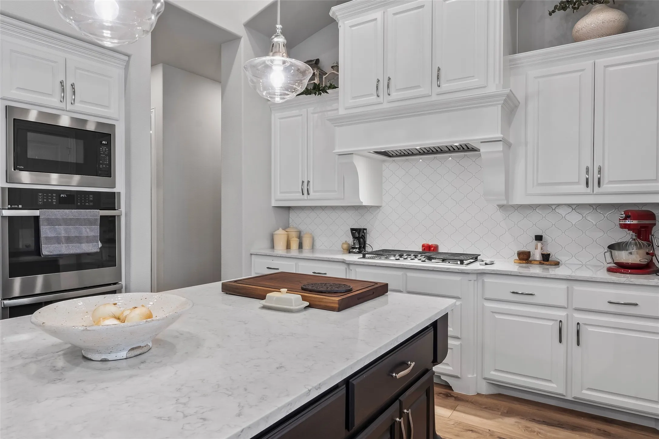 Kitchen featuring stainless steel appliances, white cabinetry, hanging light fixtures, and light wood-type flooring