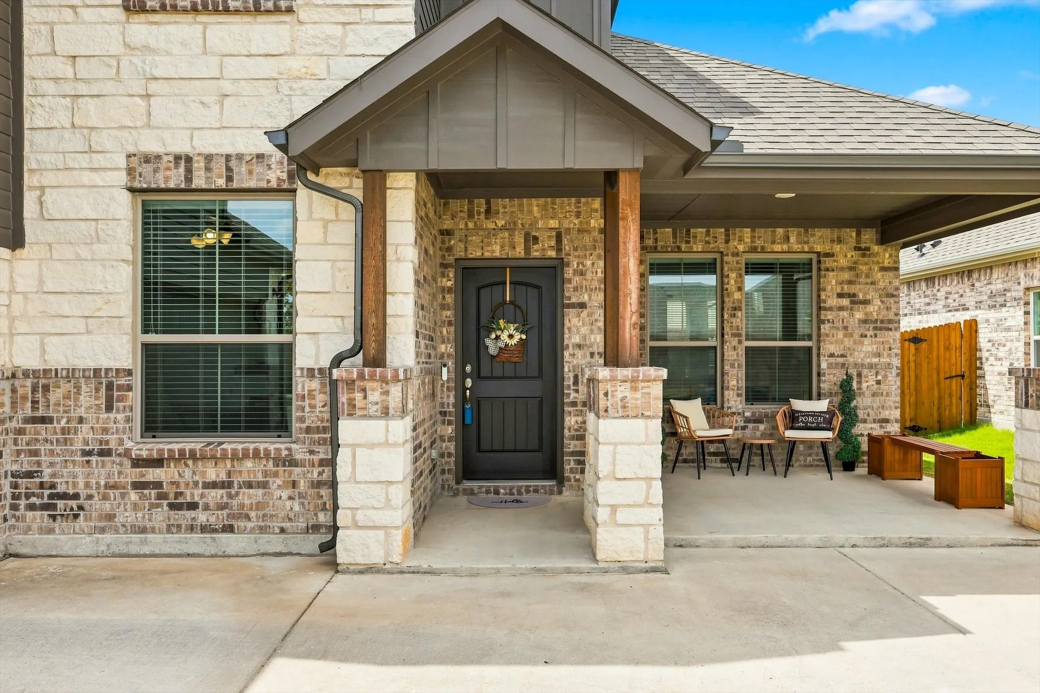 Brick and stone exterior with covered front porch, dark paneled entry door, and composition shingle roof