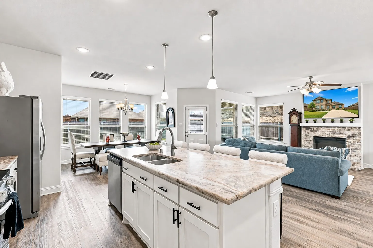 Kitchen island with dual sinks and pendant lighting, wood-finish flooring, recessed lighting, white cabinetry, and a brick fireplace