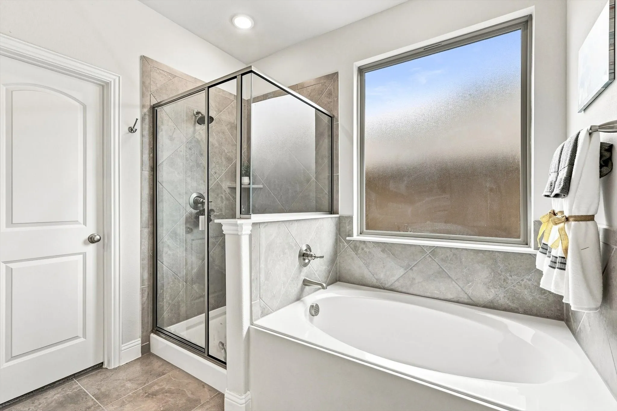 White paneled door, glass-enclosed shower with tiled walls, built-in bathtub, and a large window with privacy glass