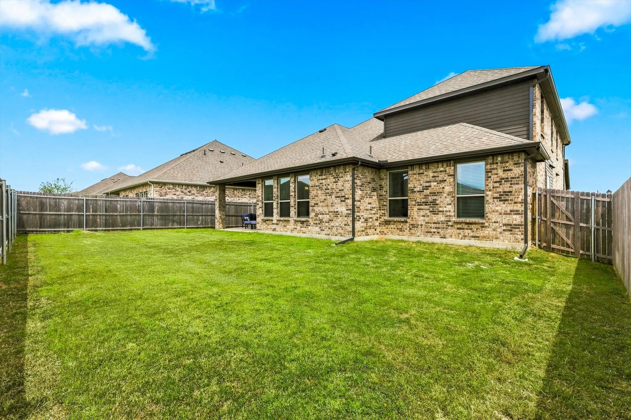 Expansive grassy yard with full privacy fencing, brick exterior, and a covered patio area