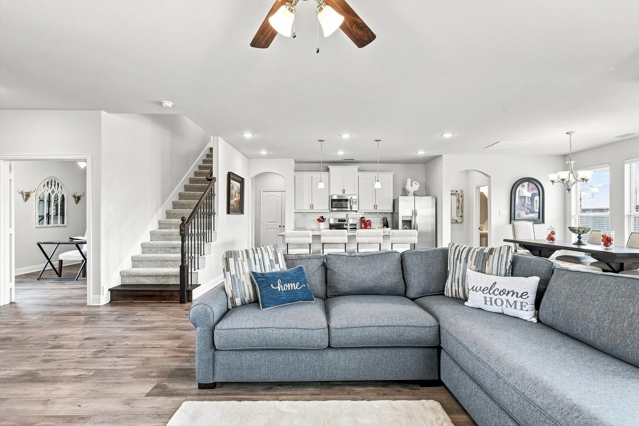 Open-concept living area featuring wood-finish flooring, recessed lighting, and a prominent staircase with dark wood newel posts and iron balusters