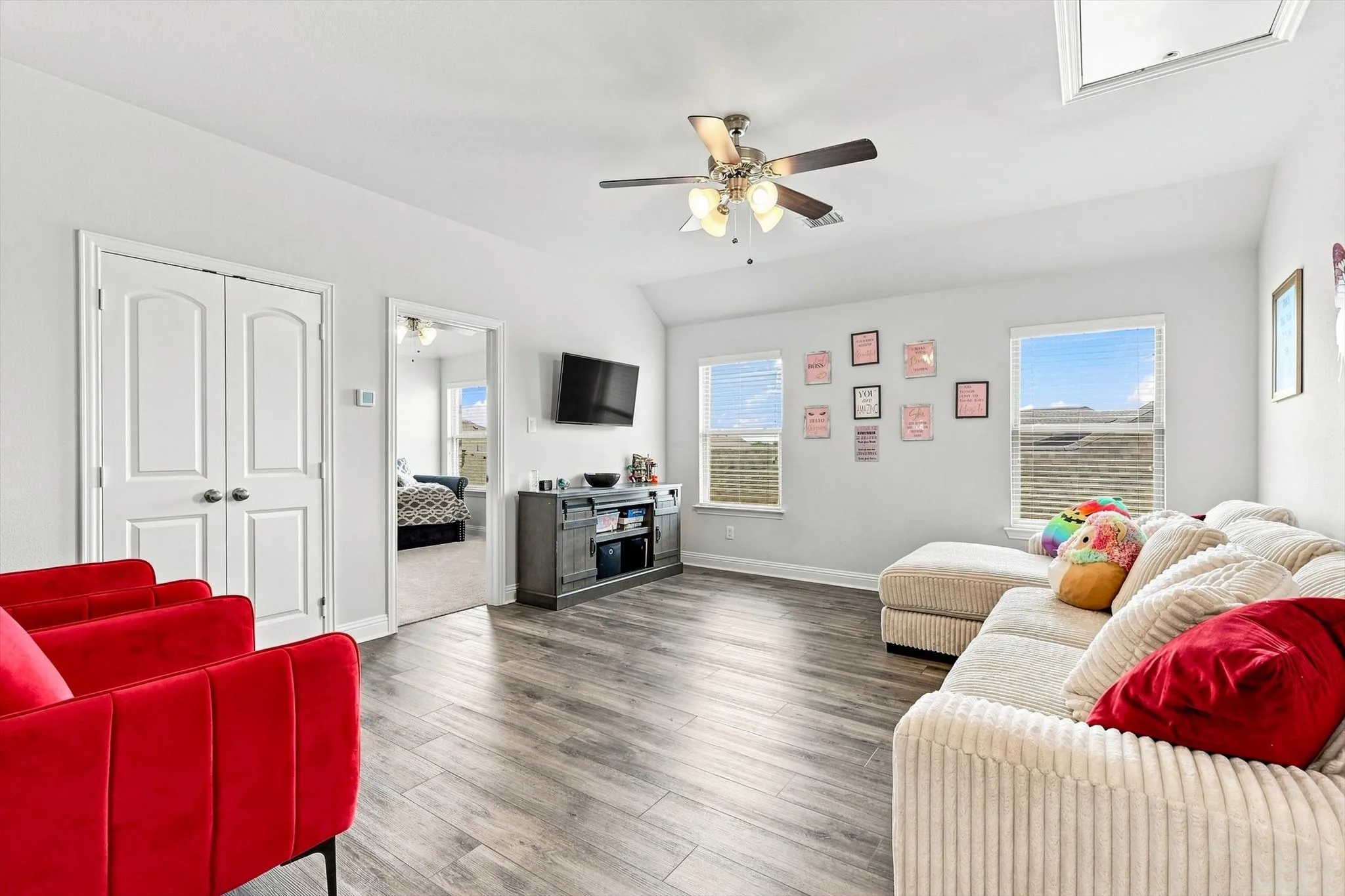 Vaulted ceilings with a ceiling fan, wood-finish flooring, two windows with blinds, and white double doors