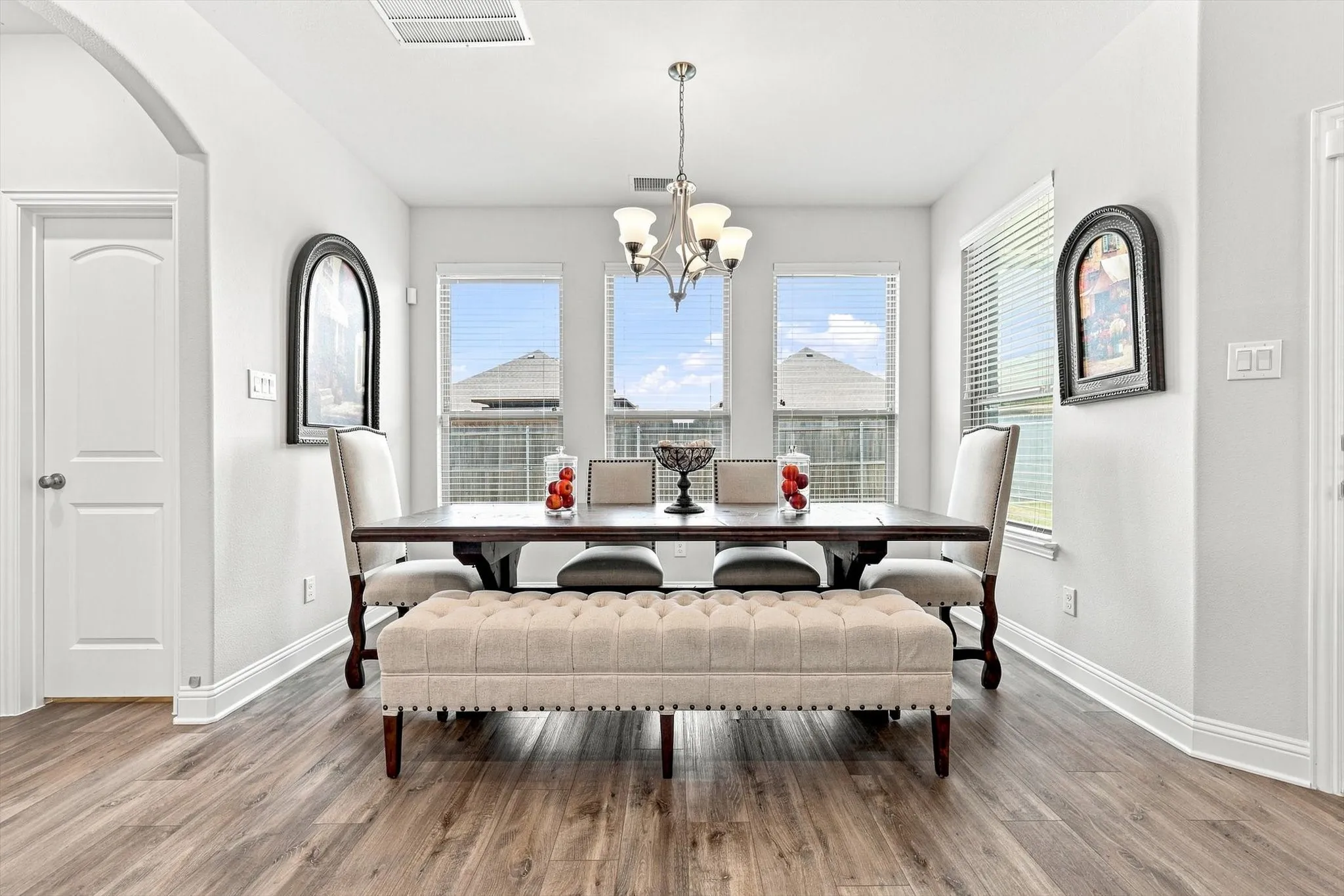 Wood-finish flooring, white trim, arched doorway, three large windows, and a chandelier with glass shades