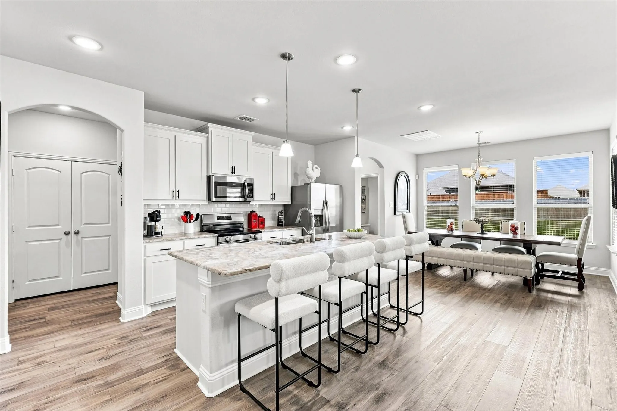 Open-concept kitchen with a large central island, white cabinetry, a subway tile backsplash, and stainless steel appliances