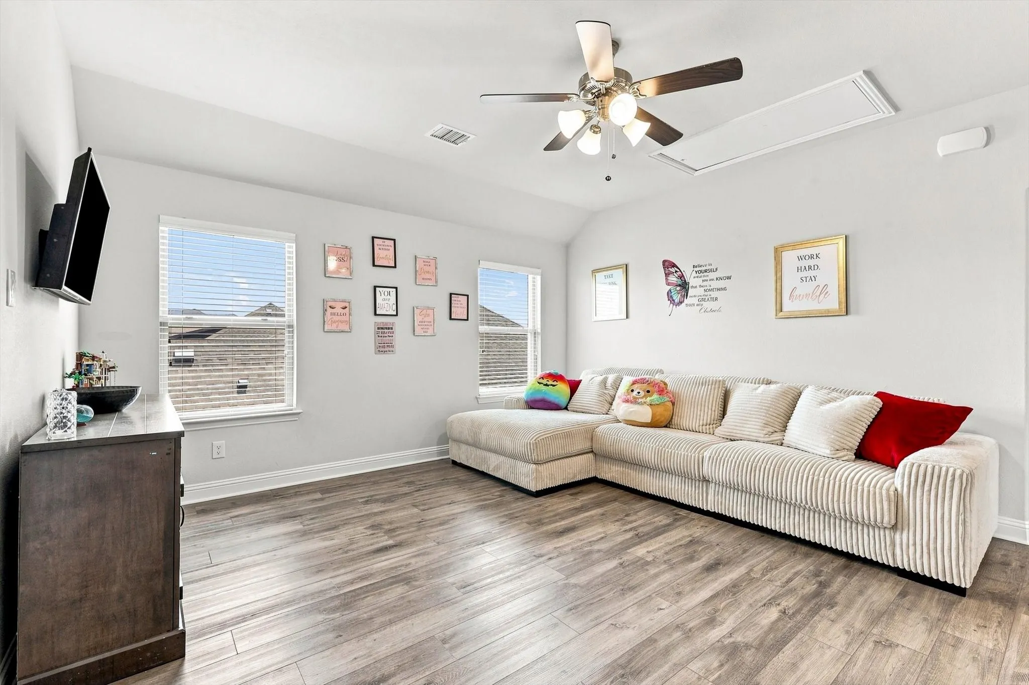 Wood-finish flooring throughout, light-colored walls, multiple windows with blinds, and a ceiling fan with integrated lighting