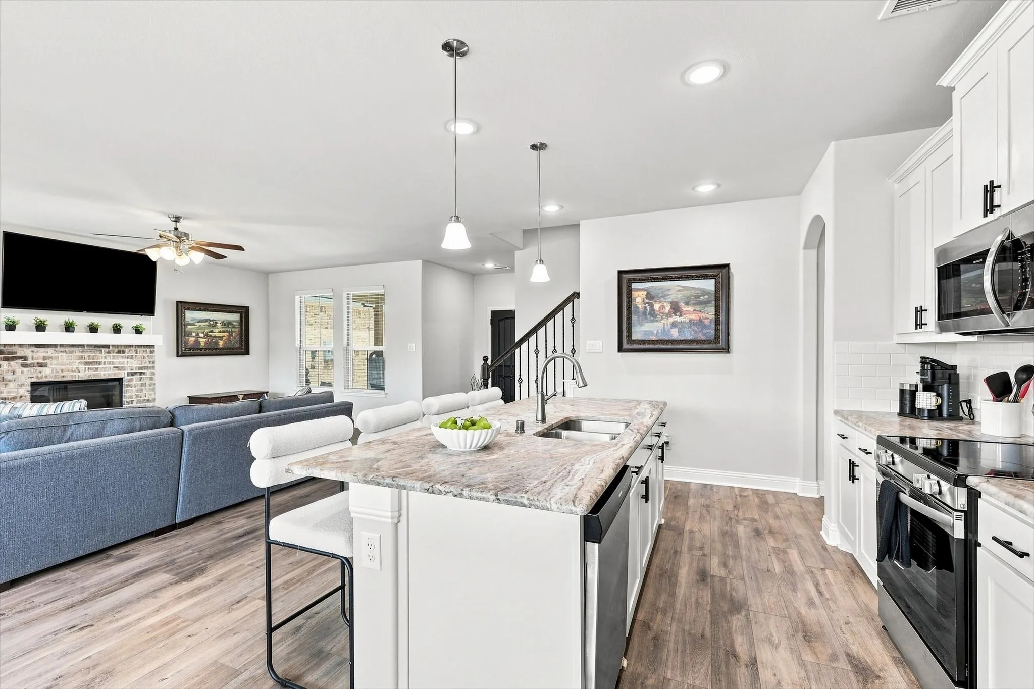 Kitchen with white shaker cabinetry, stainless steel appliances, and a central island with a double basin sink and pendant lighting