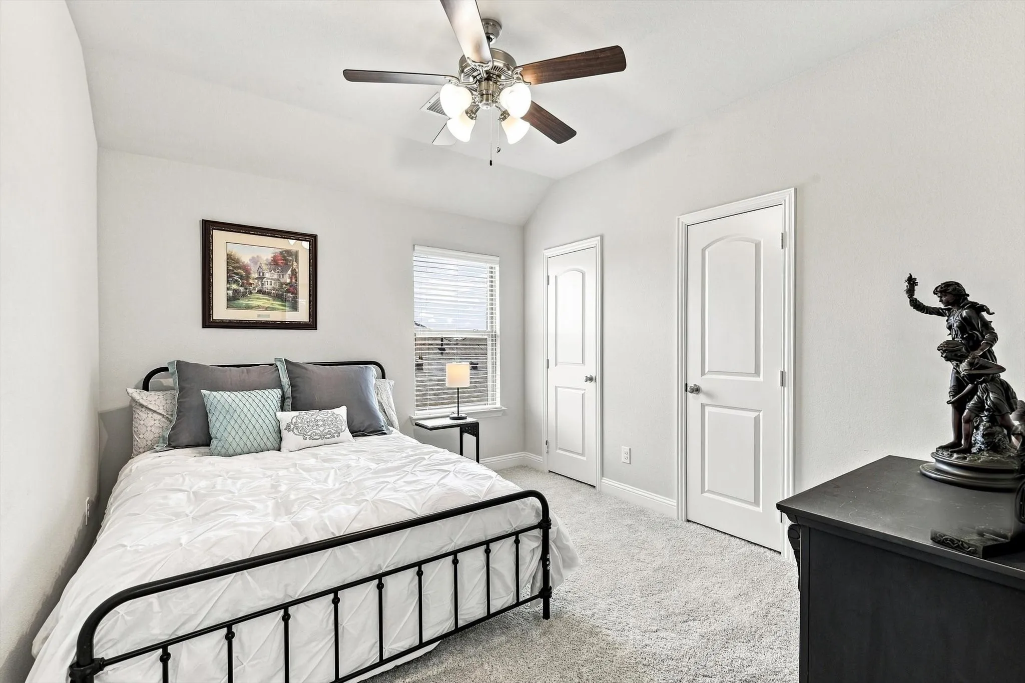 Vaulted ceiling, two paneled doors, window with blinds, ceiling fan with light fixture, and carpeted flooring