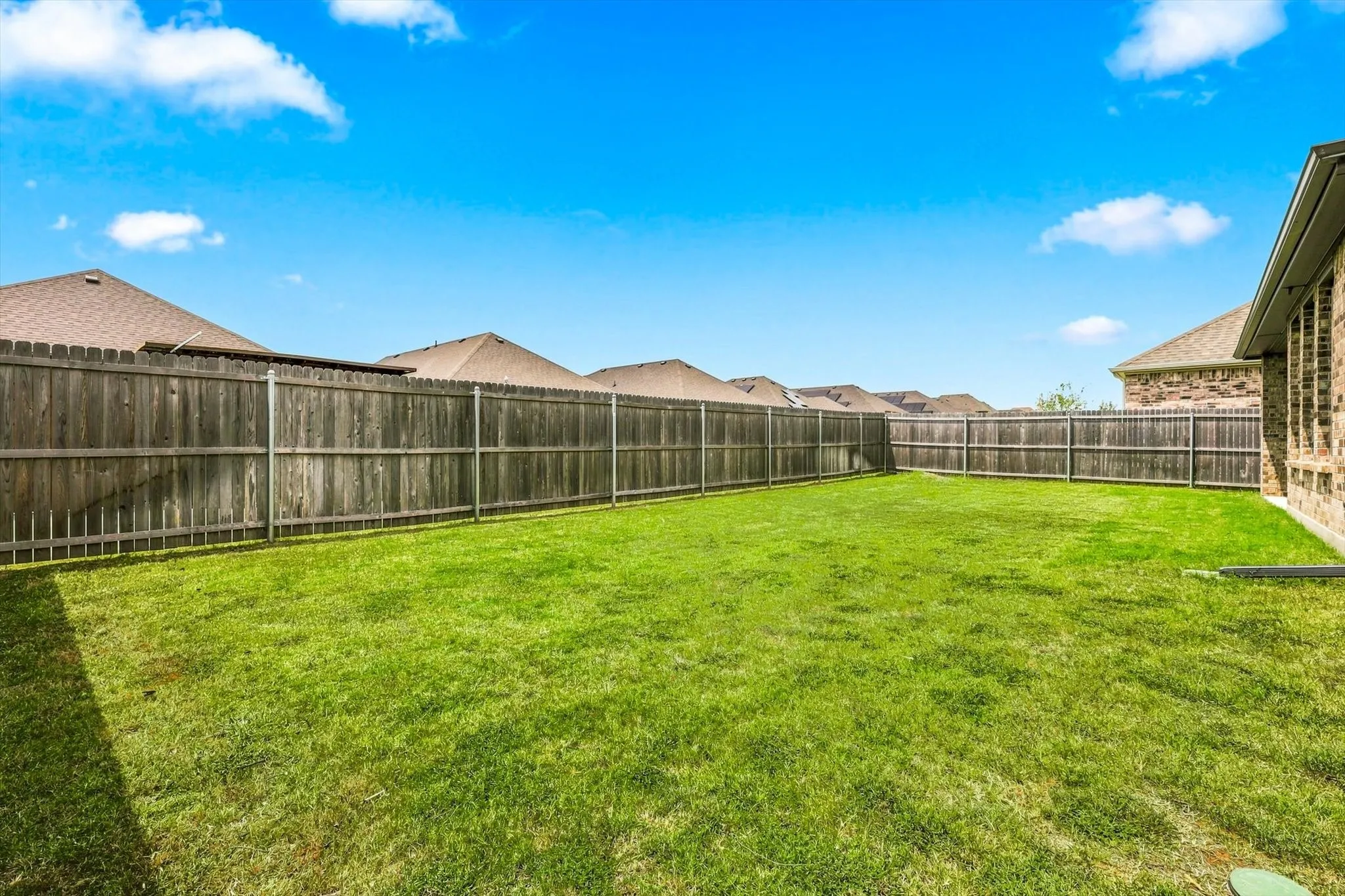 Expansive backyard with a manicured lawn, full privacy fencing, and brick exterior
