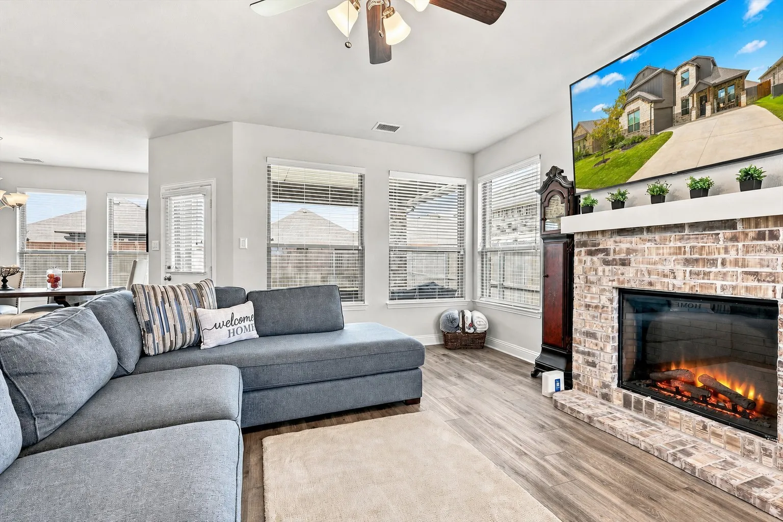 Spacious living area featuring wood-finish flooring, a brick-surround fireplace, and multiple windows with blinds