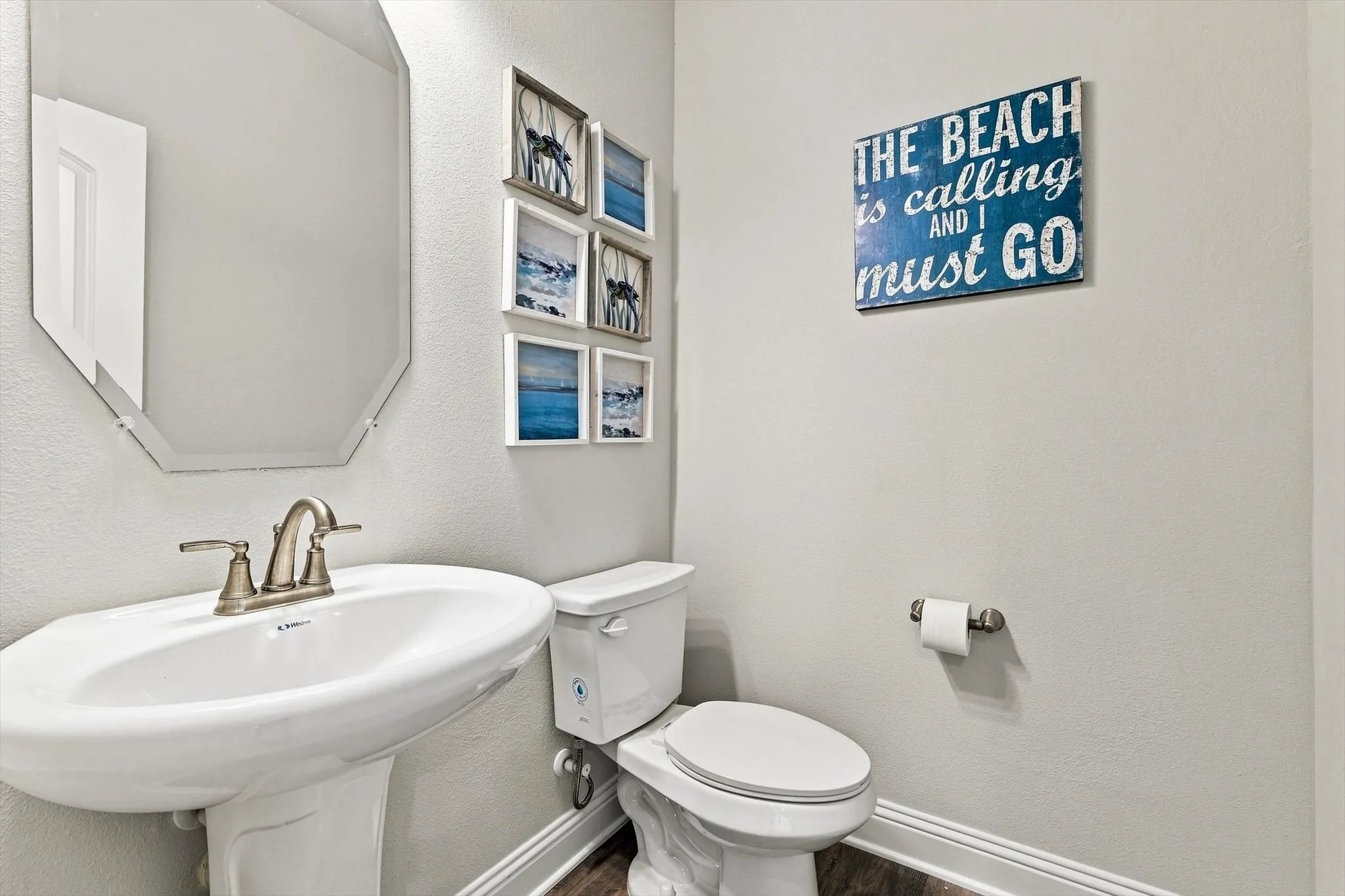 Pedestal sink with a brushed nickel faucet, octagonal mirror, and white toilet