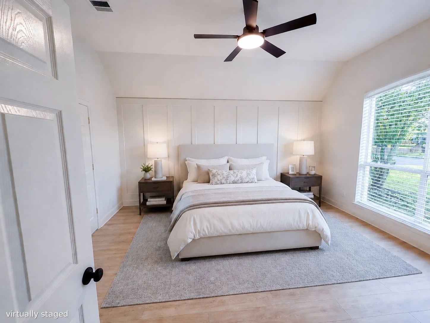 Bright, spacious primary bedroom with vaulted ceilings, modern ceiling fan, large picture window, and designer accent wall.