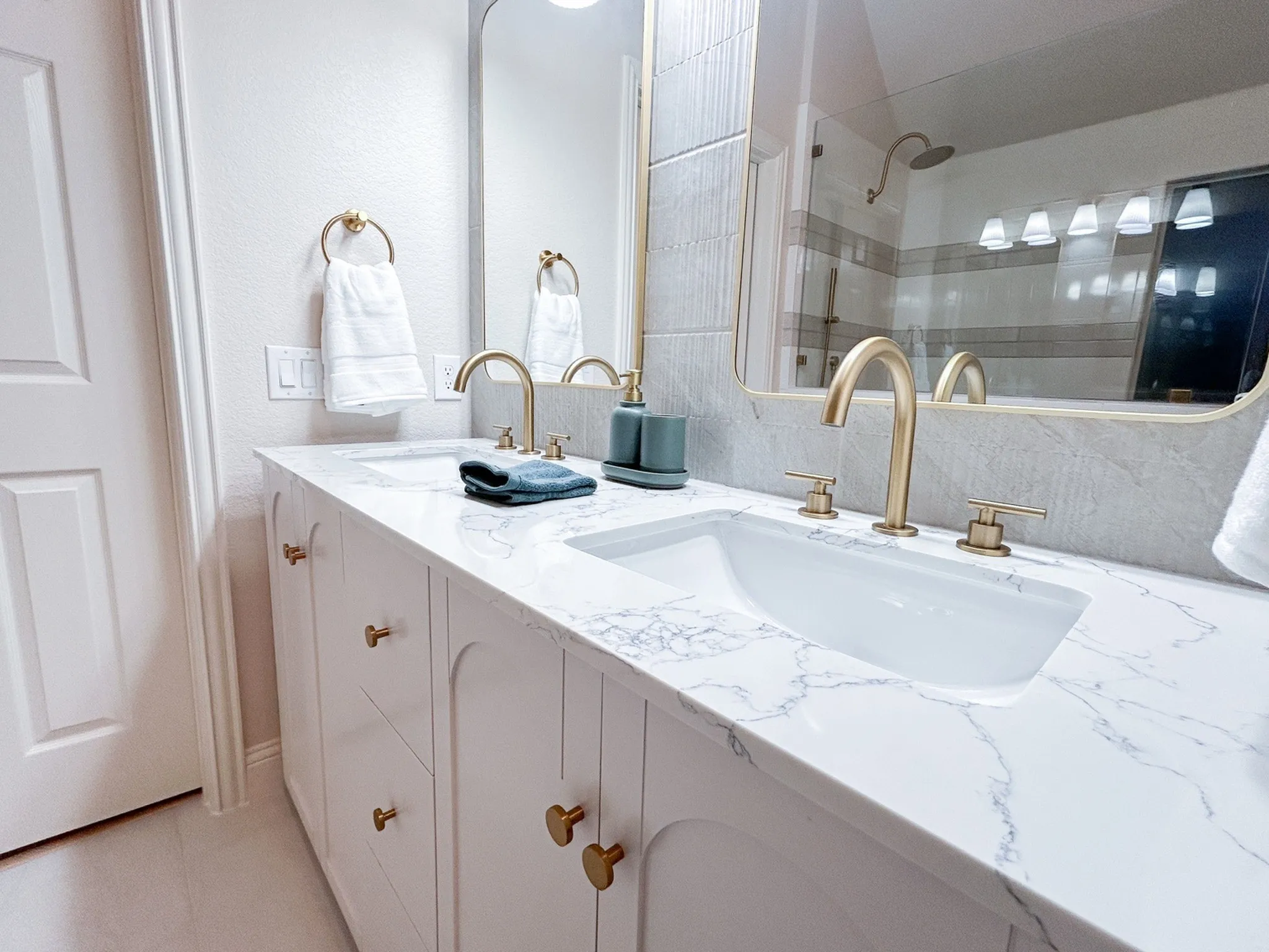 Elegant dual-sink vanity with marble-look countertops, custom cabinetry, designer brass fixtures, and abundant storage.