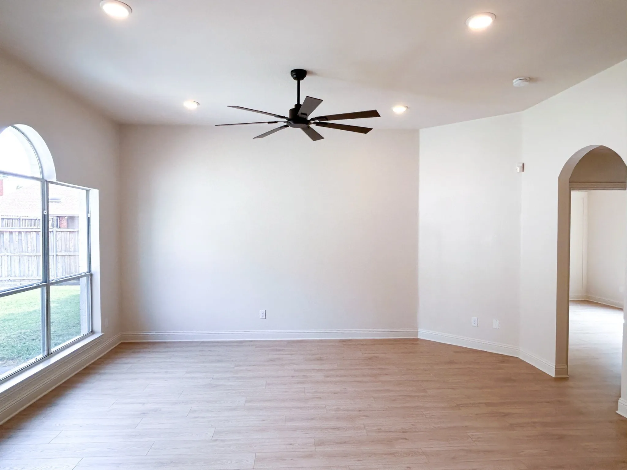 Spacious living room with soaring ceilings, wood flooring, arched window, and abundant natural light.