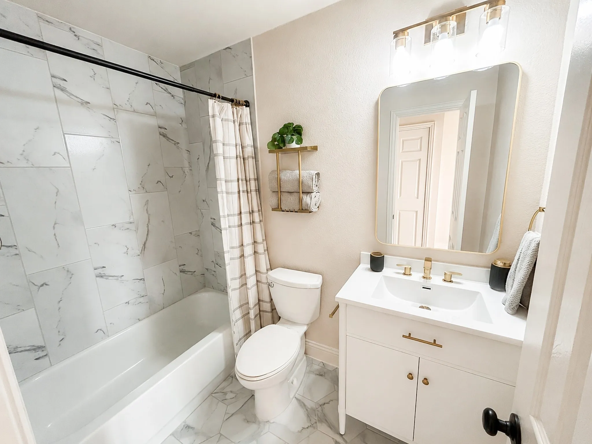 Beautifully updated secondary bathroom with marble-look tile, a modern vanity, brass fixtures, and a tub/shower combination.
