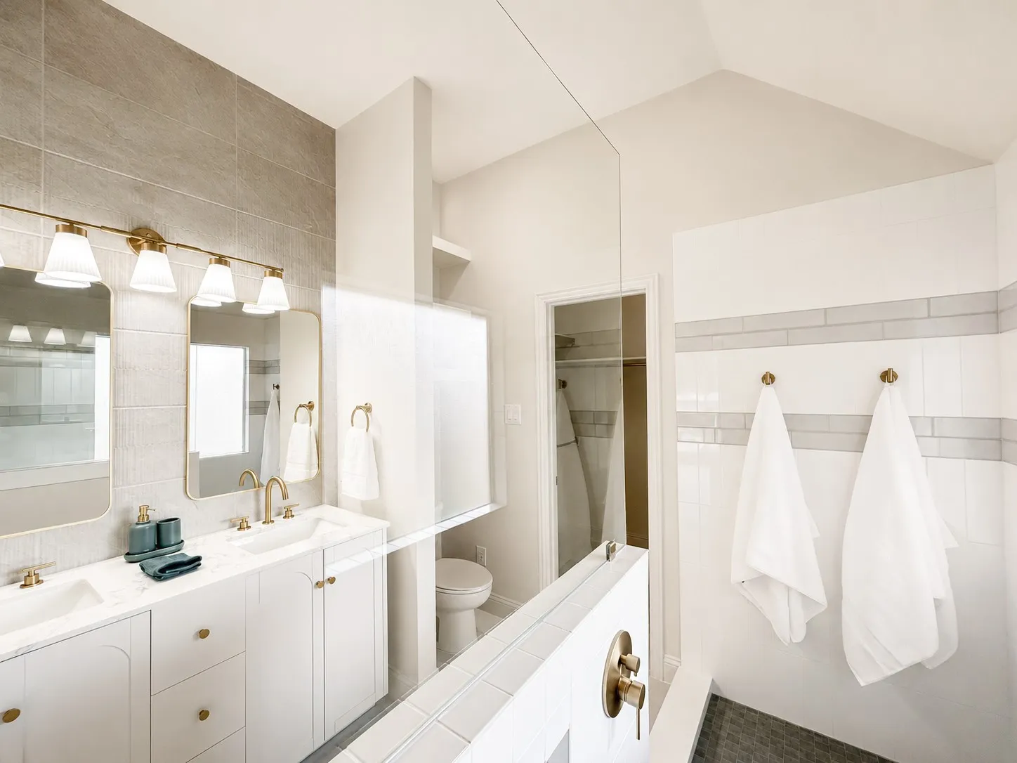 Bright, spa-like primary bathroom with dual vanities, elegant brass fixtures, statement tile, and a beautifully tiled walk-in shower.